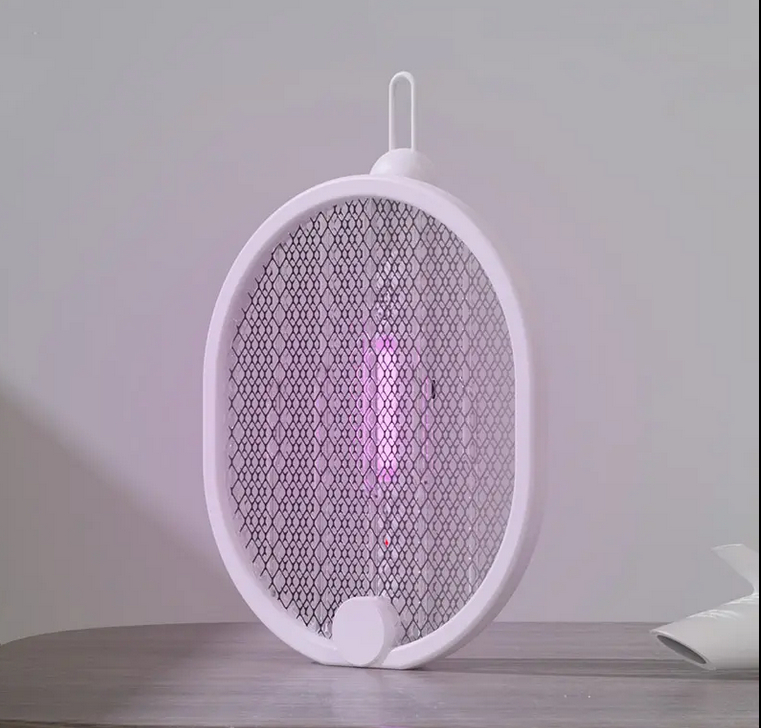 Weißer Insektenvernichter mit ovalem Rahmen, Netzgitter und Griff. Violettes Licht geht von der Mitte aus. Auf einem Tisch.