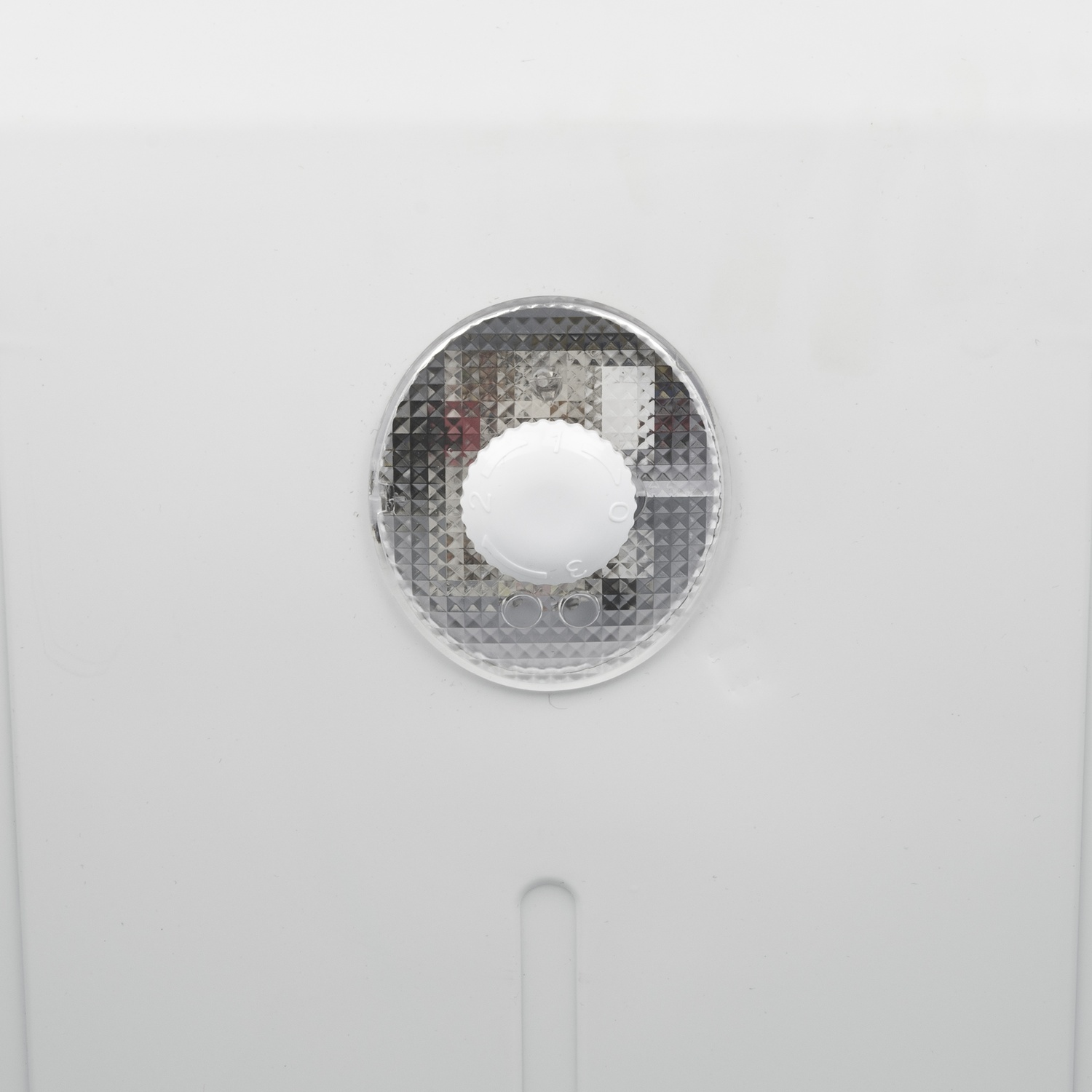 Primo piano di un quadrante di controllo bianco con numeri, inserito in una copertura trasparente. Lo sfondo è una superficie bianca con una fessura.