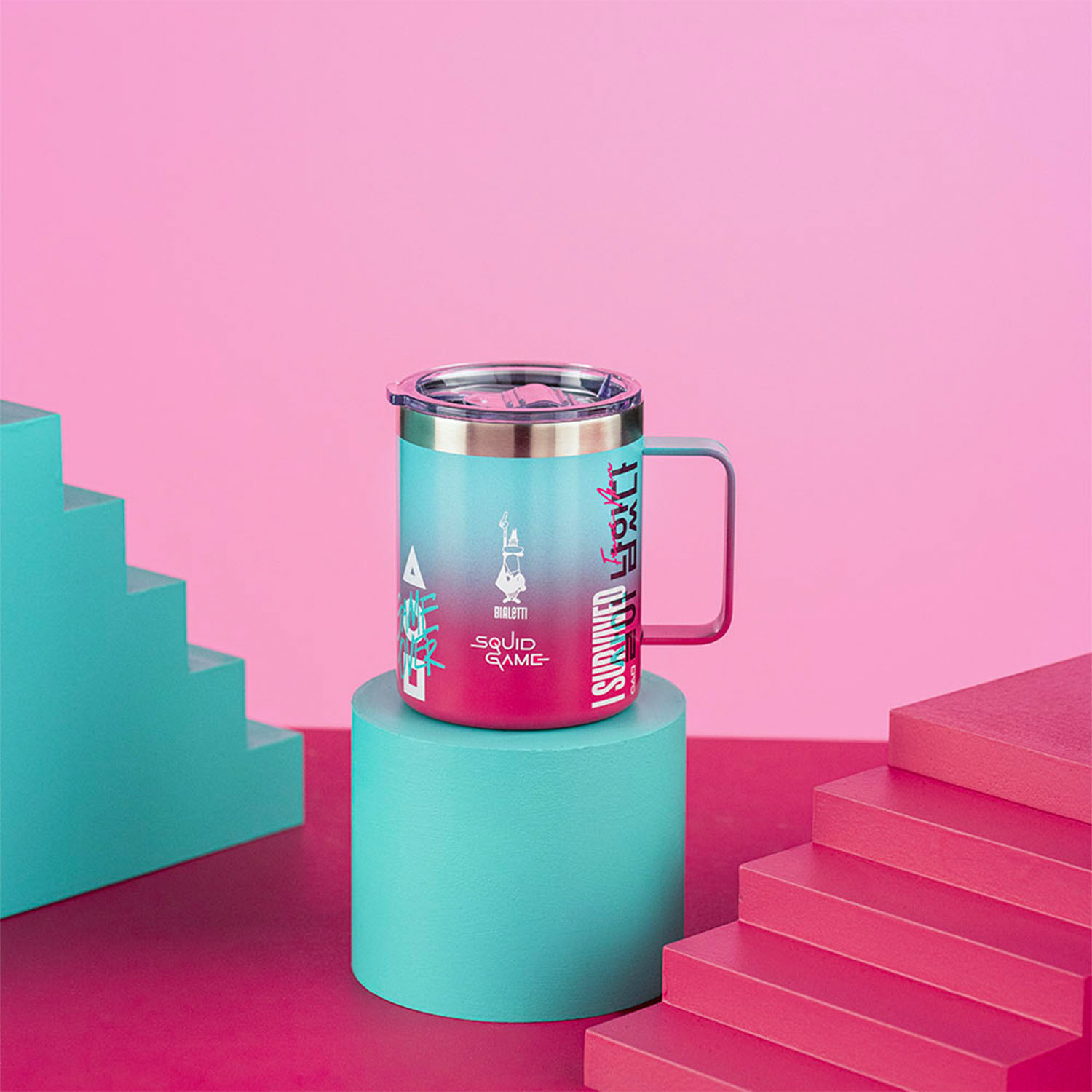 Una tazza con 'Squid Game' è appoggiata su un cilindro turchese. Scale rosa e sfondo rosa incorniciano la scena.