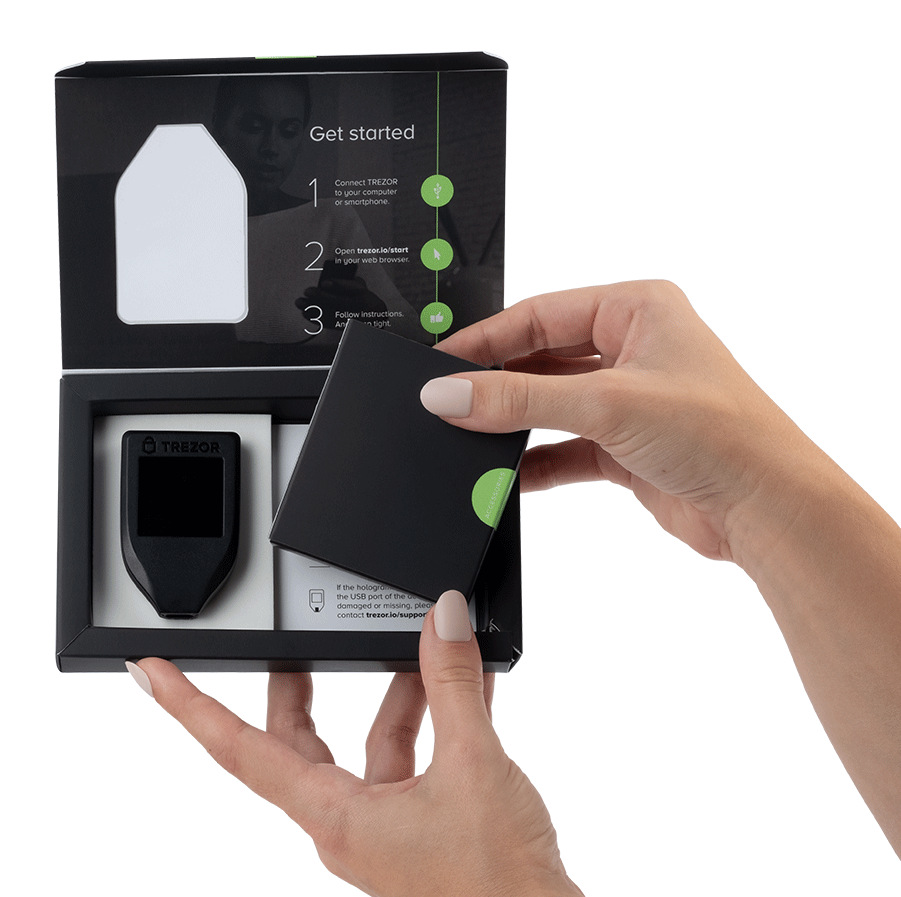 Osoba otwiera czarne pudełko zawierające czarne urządzenie Trezor. Pudełko zawiera instrukcje i akcesoria, na białym tle.