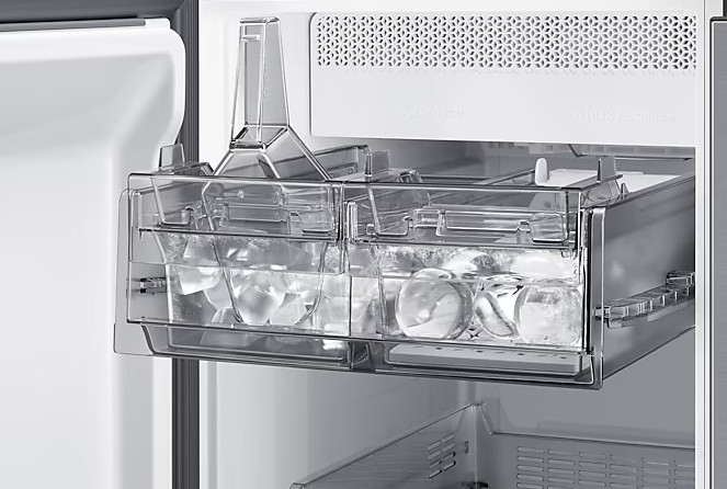 Przezroczysta kostkarka do lodu w lodówce. Tacka na kostki lodu wypełniona lodem. Przezroczyste elementy z tworzywa sztucznego. Białe tło.