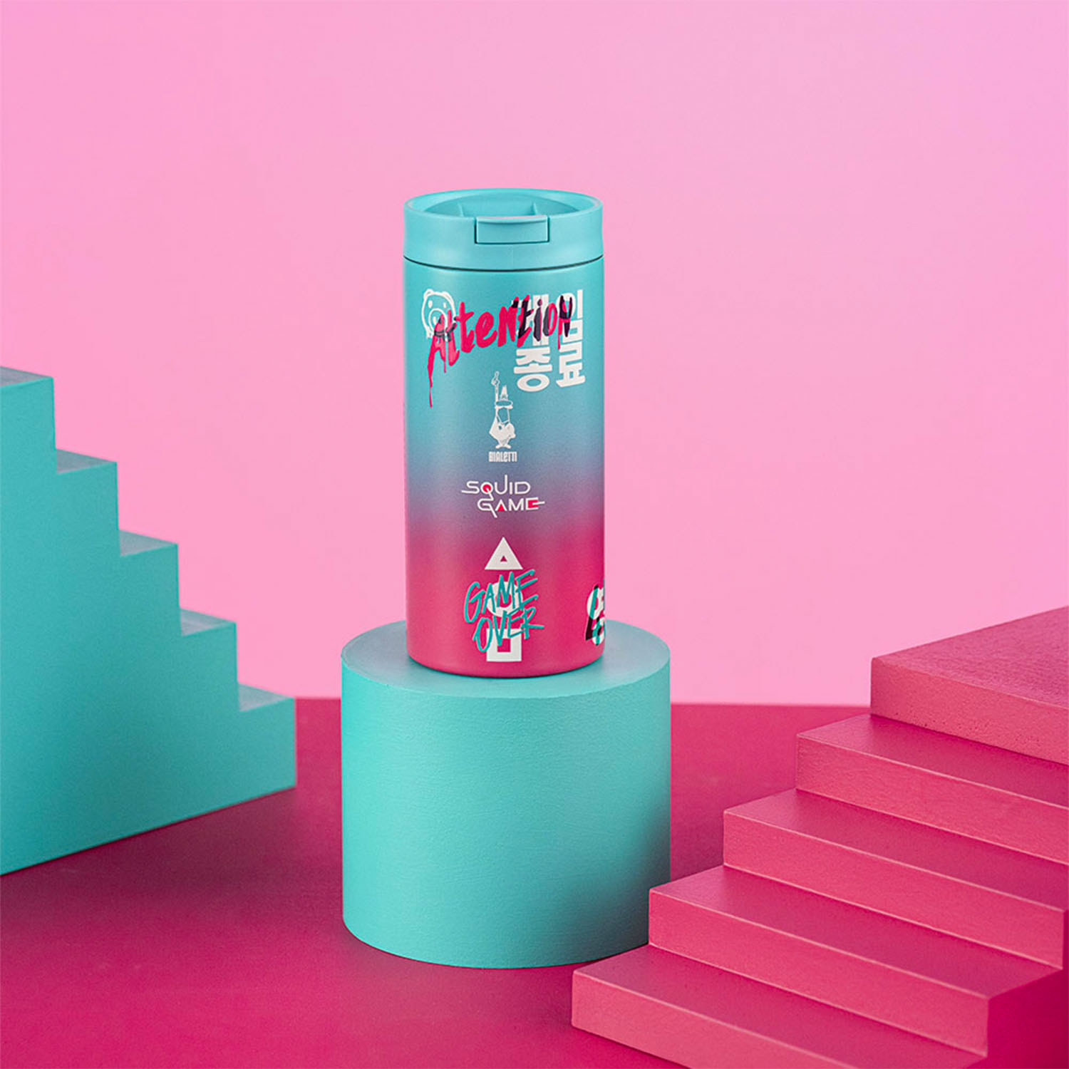Una borraccia a tema Squid Game su un cilindro turchese, sfondo rosa e strutture a forma di scala.