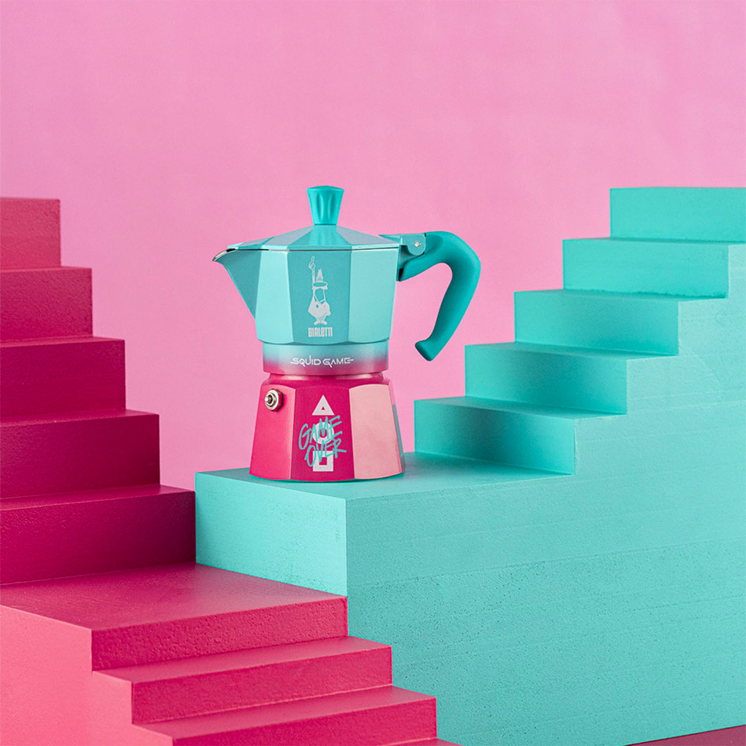 Una caffettiera Bialetti di Squid Game colorata sulle scale. Gradini ciano, rosa e rossi. Sfondo rosa.