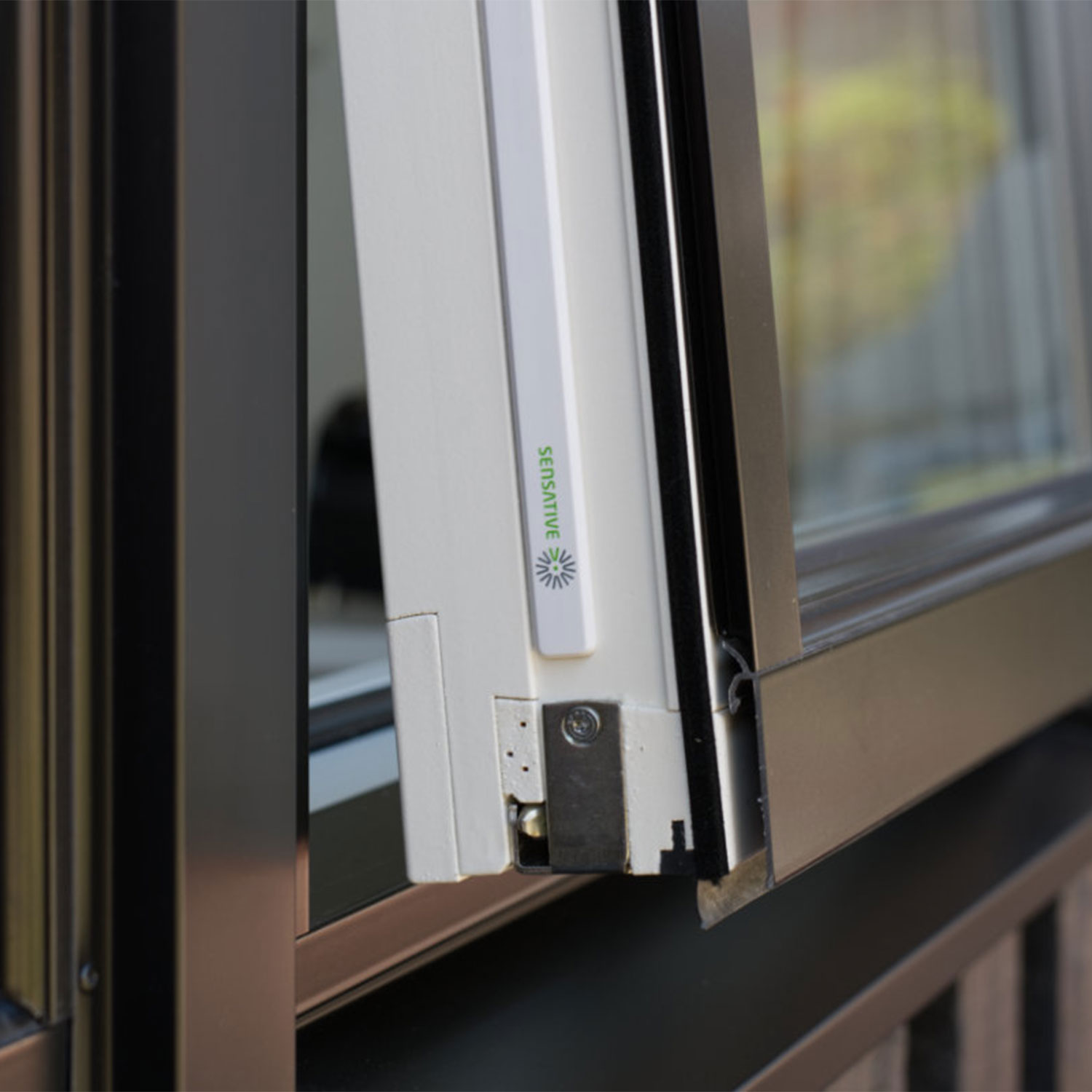 Nahaufnahme eines Fensterrahmens. Weißer Rahmen mit der Aufschrift 'SENSATIVE'. Schwarzer Rahmen um das Glas und ein Metallteil mit Schraube.