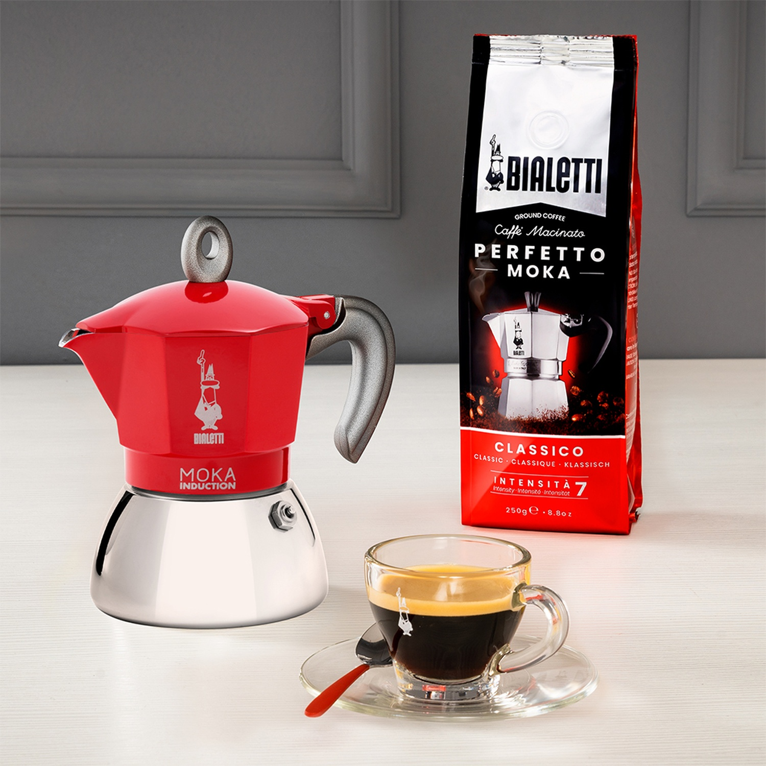 Una caffettiera moka Bialetti rossa, un sacchetto di caffè e una tazza di caffè su un tavolo.