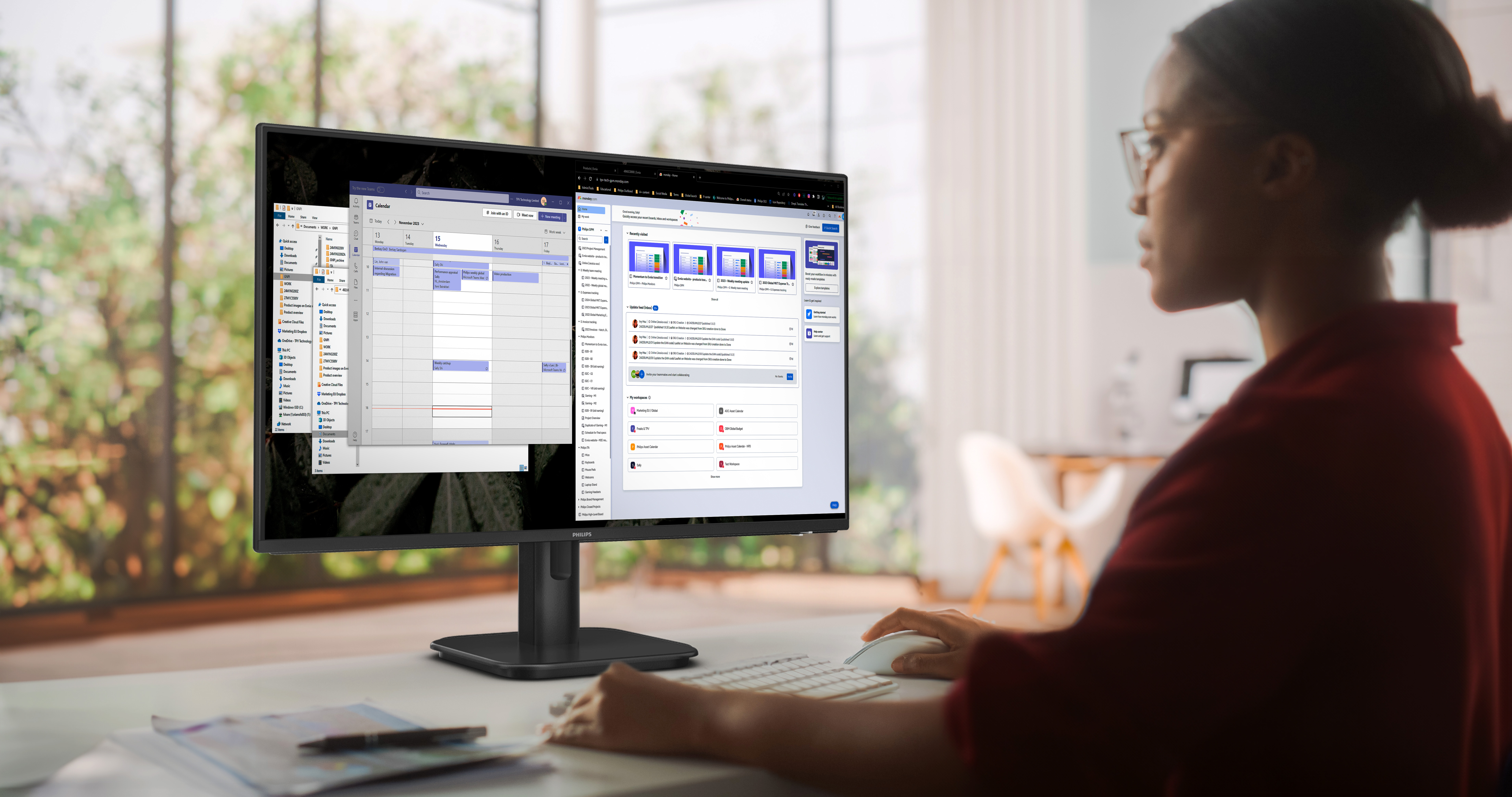 Frau benutzt Computer mit Kalender auf dem Bildschirm. Schreibtisch mit Tastatur und Maus. Hintergrund mit Fenster und Bäumen.