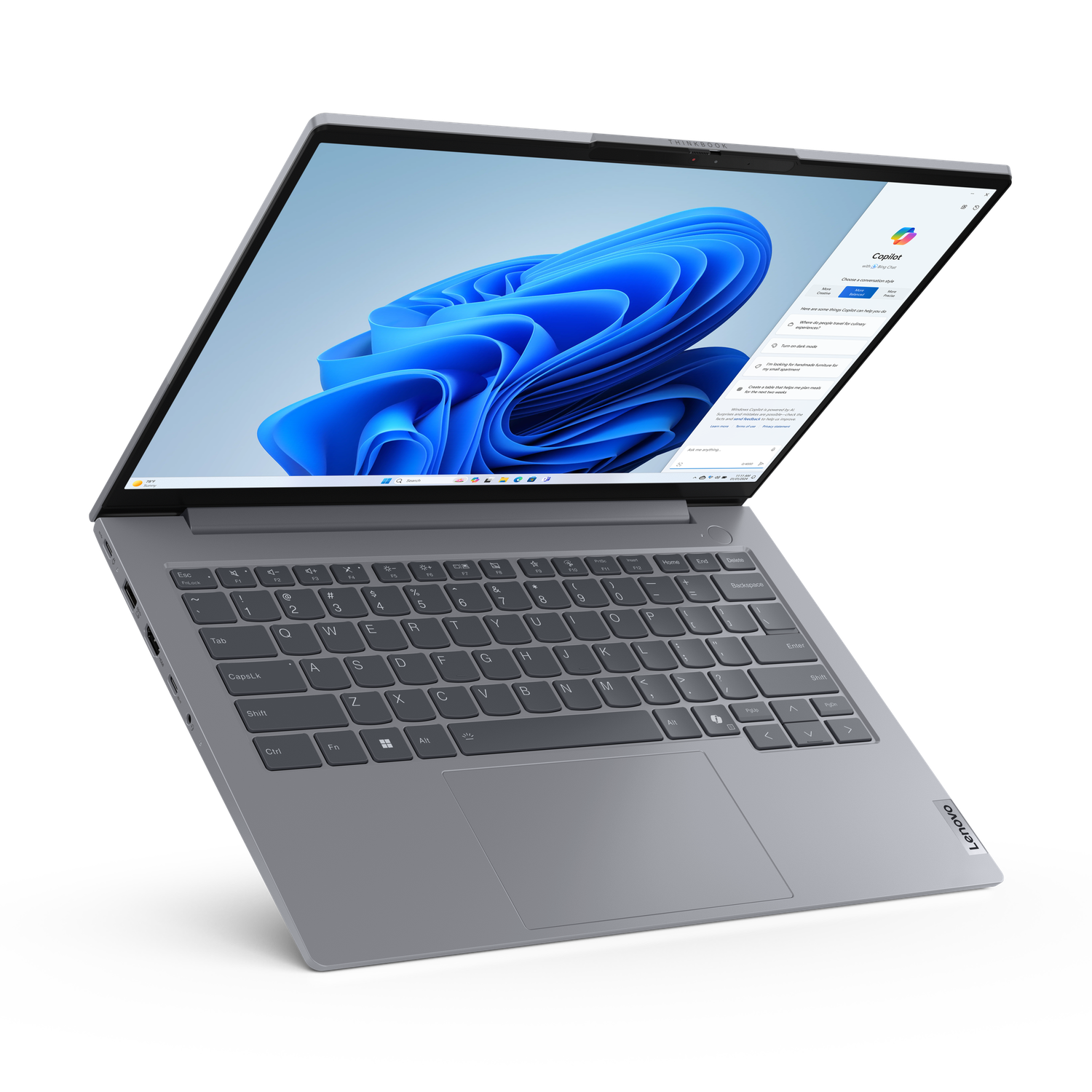A gray Lenovo laptop is open, displaying Windows 11. The screen shows a blue abstract image and the Copilot interface.