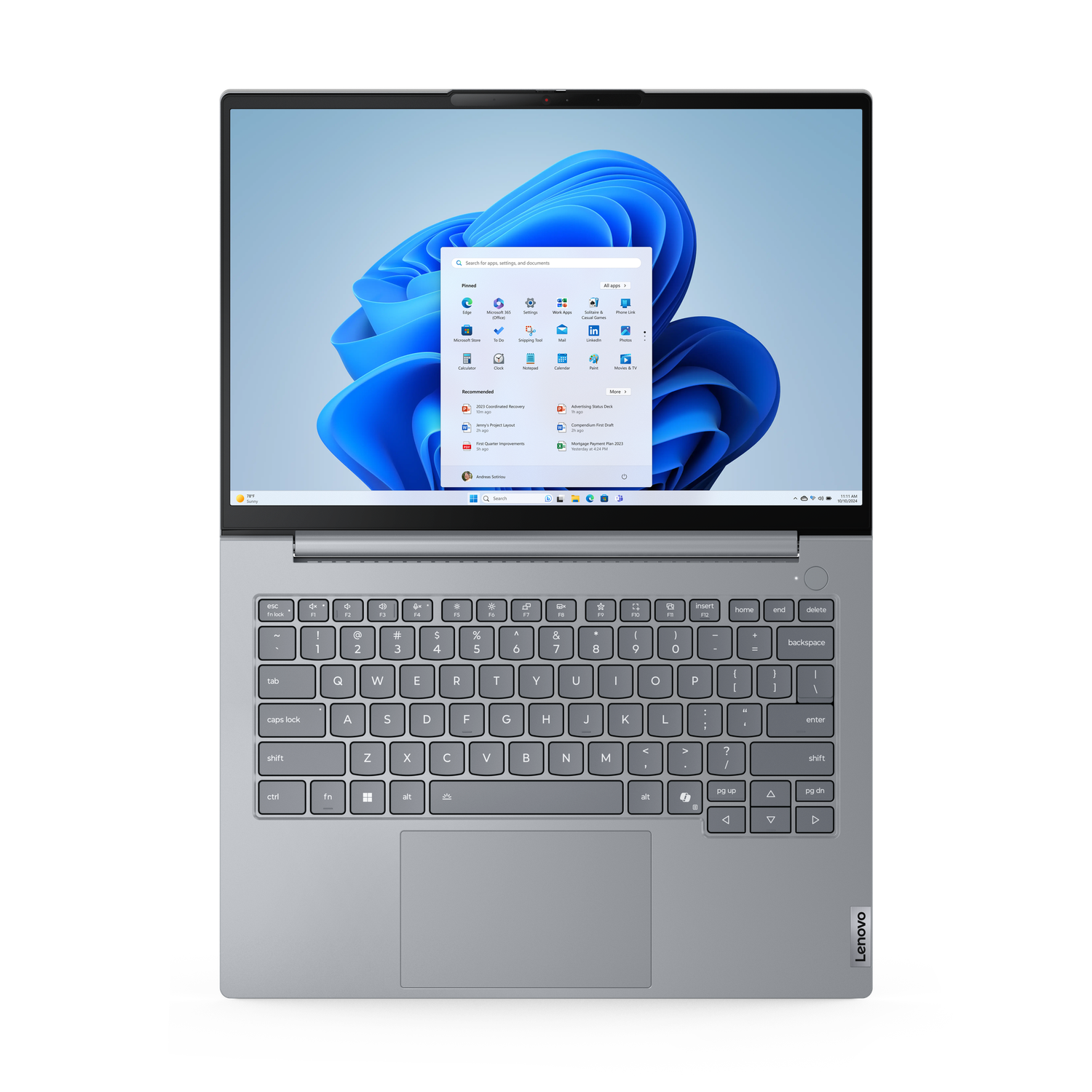 Laptop on a black surface, screen displaying Windows 11 interface. The keyboard is visible. Lenovo logo is on the bottom right.