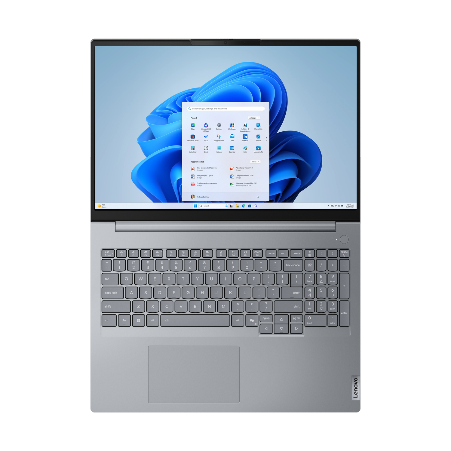 Zilveren laptop met Windows 11-interface. Scherm toont app-pictogrammen. Toetsenbord zichtbaar. Lenovo-logo rechts.