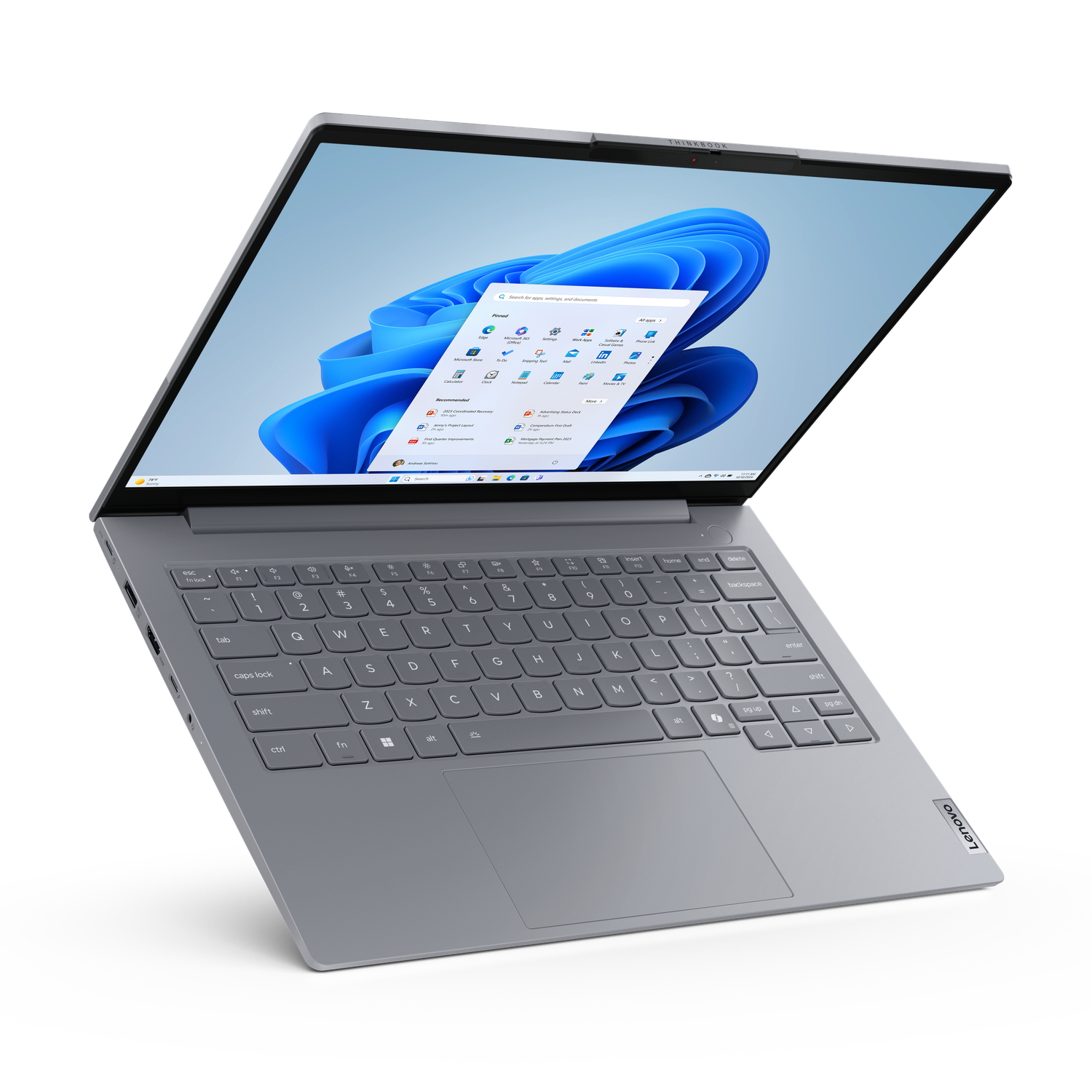 A silver Lenovo laptop is open. The screen displays a Windows 11 interface. Keyboard visible, with the Lenovo logo in the corner.