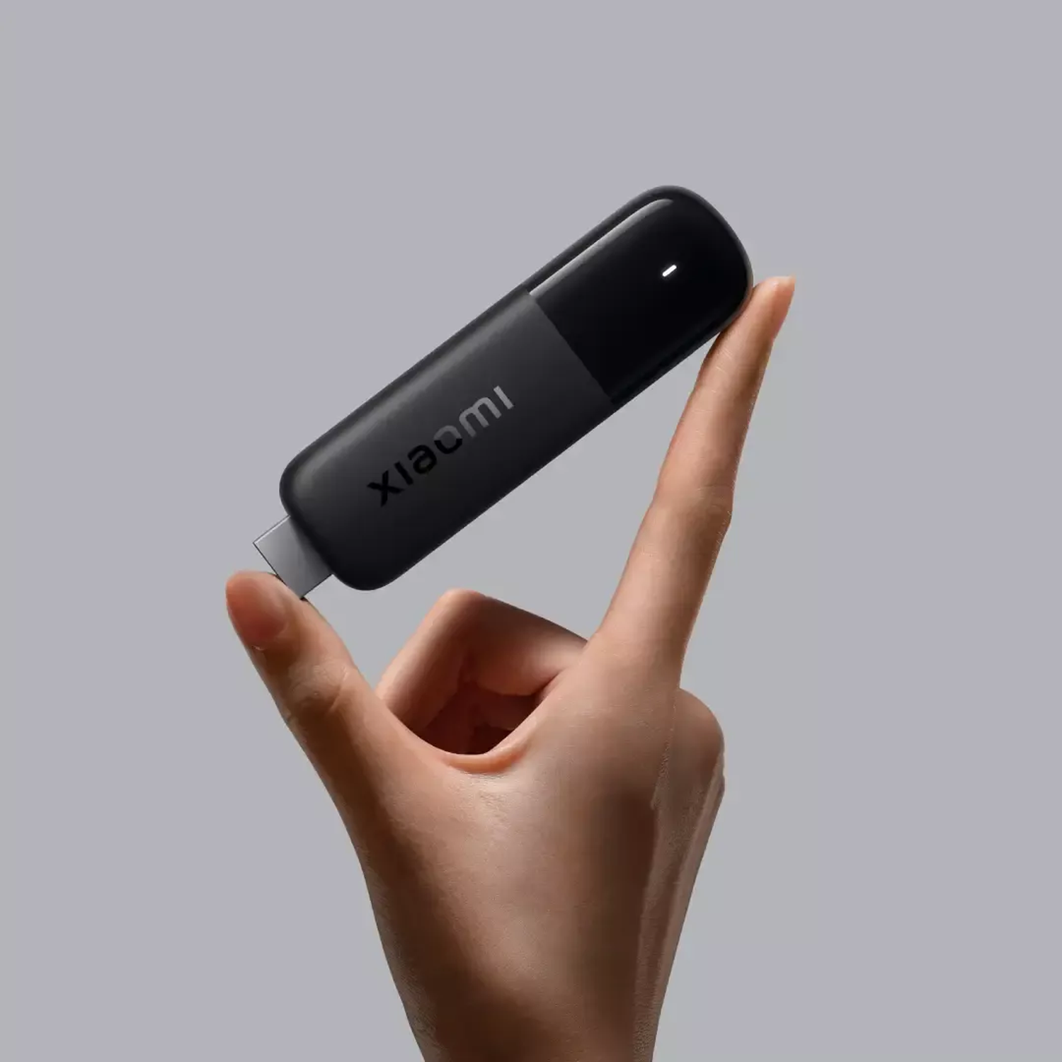 Een hand houdt een zwarte Xiaomi USB-apparaat tegen een lichtgrijze achtergrond. Het apparaat heeft het Xiaomi-logo en een klein wit licht.