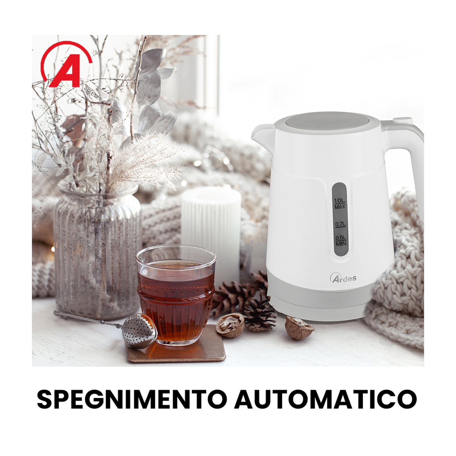 Un bollitore elettrico bianco accanto a un bicchiere di tè. Un infusore per tè, noci ed elementi decorativi sul tavolo.