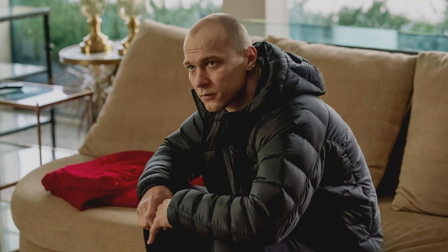 Ein Mann in einer schwarzen Daunenjacke sitzt auf einer Couch neben einem roten Pullover.