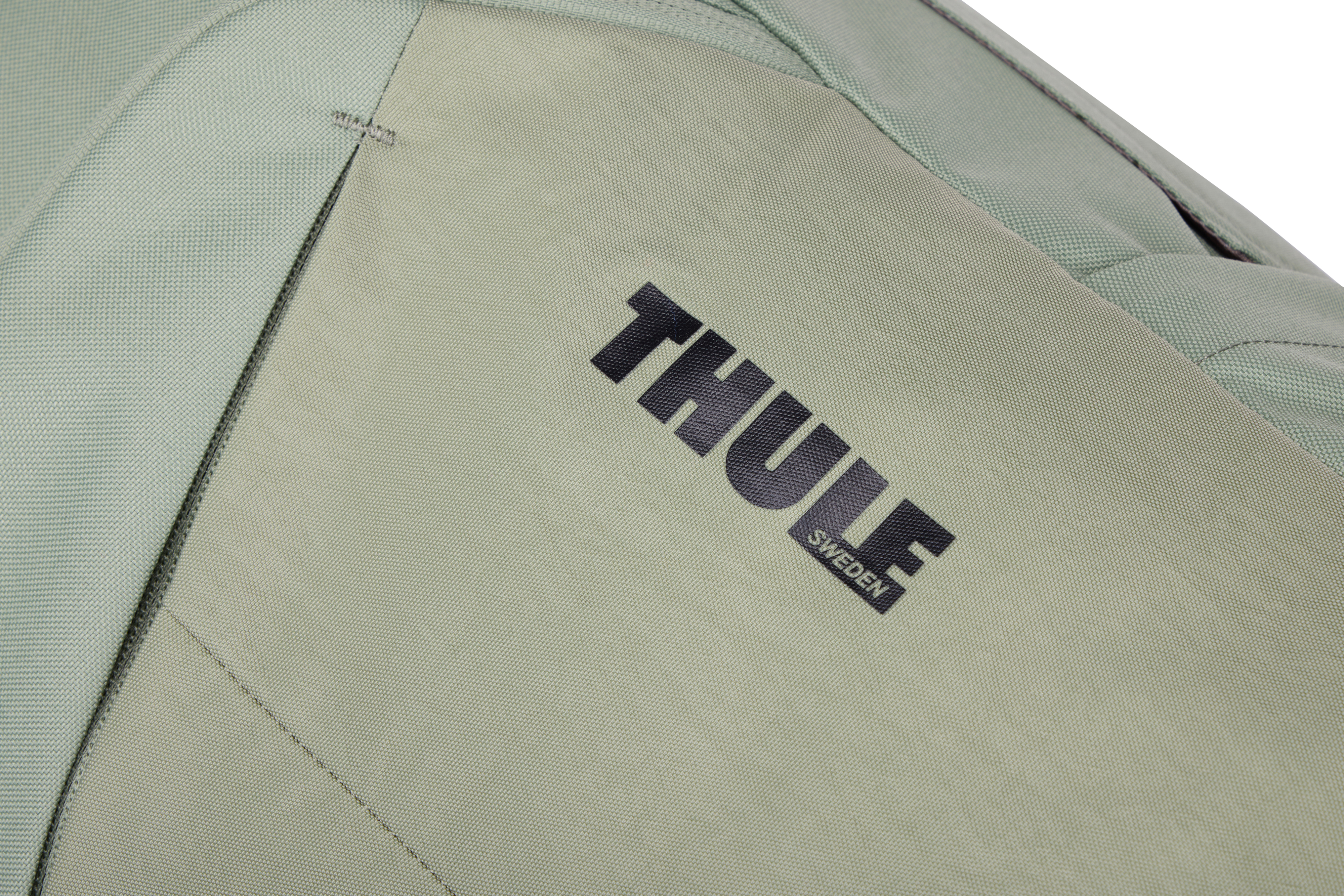 "THULE SWEDEN" siyah logolu, adaçayı yeşili bir çantanın yakın çekimi. Çantanın dikişli dikişleri ve dokulu bir kumaşı var.