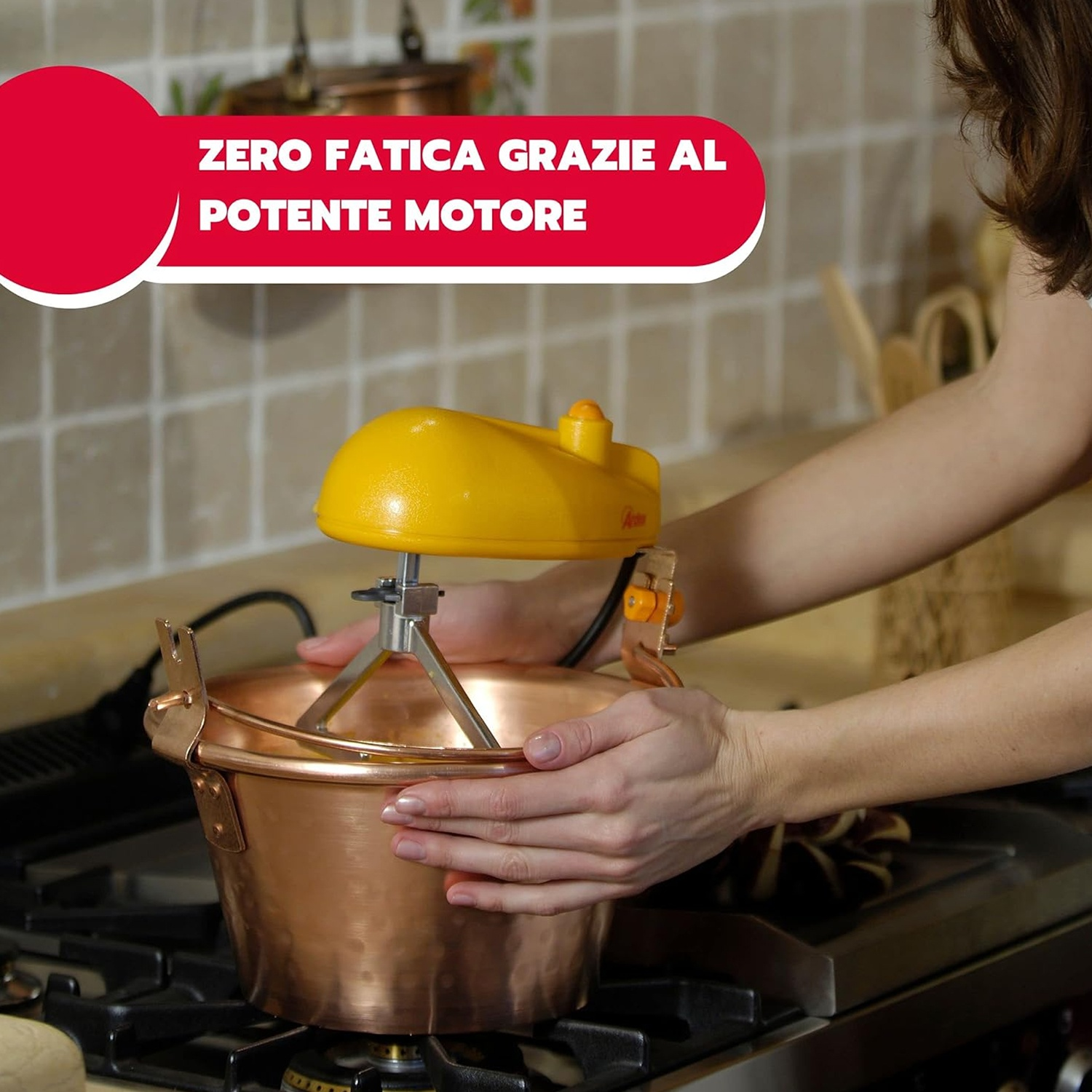 Una donna usa un elettrodomestico giallo per mescolare una pentola di rame su un fornello. Il testo in alto dice 'Zero fatica grazie al potente motore'.