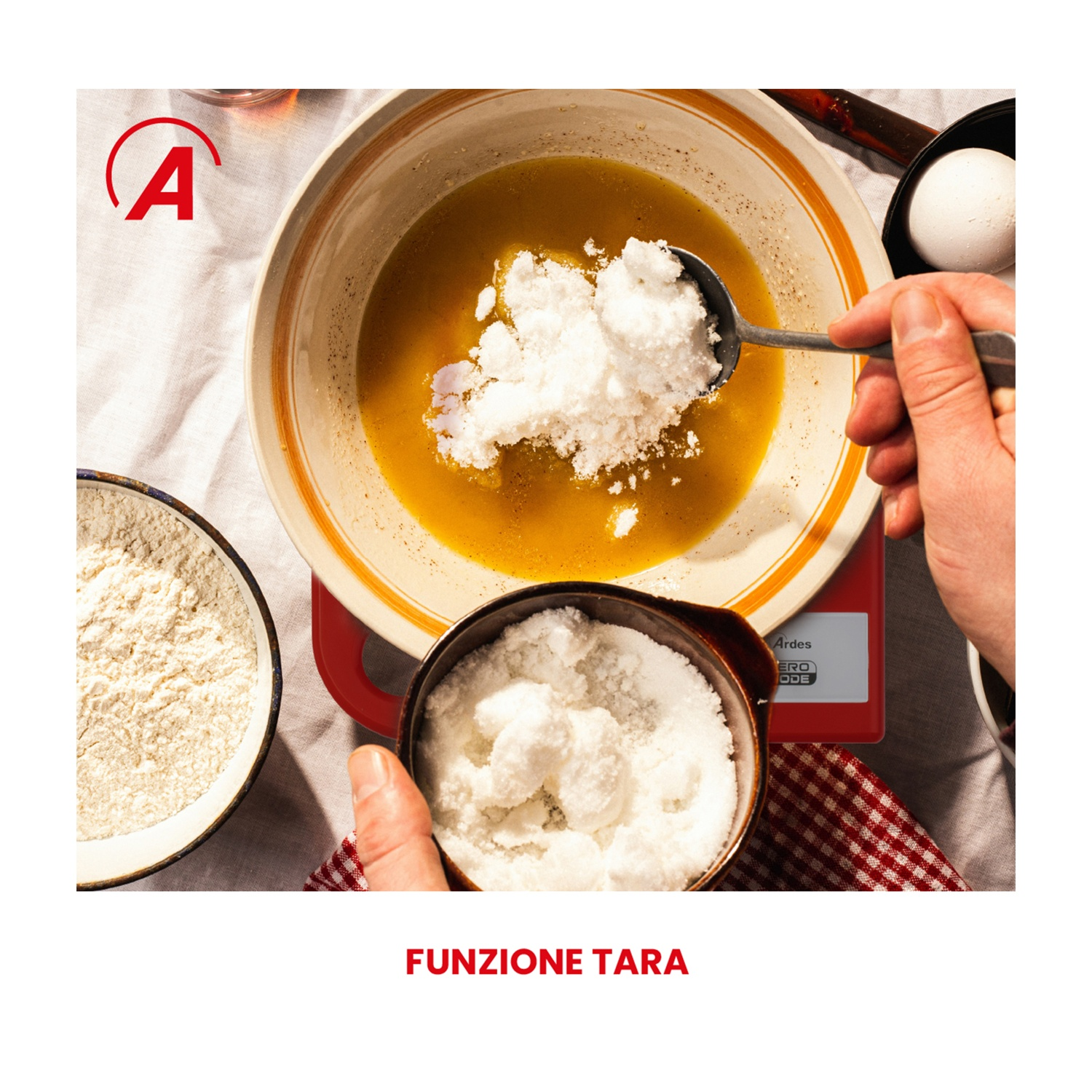 Una persona aggiunge zucchero a una ciotola con liquido usando un cucchiaio. Sono presenti altre ciotole con farina e zucchero, un uovo e una bilancia rossa.