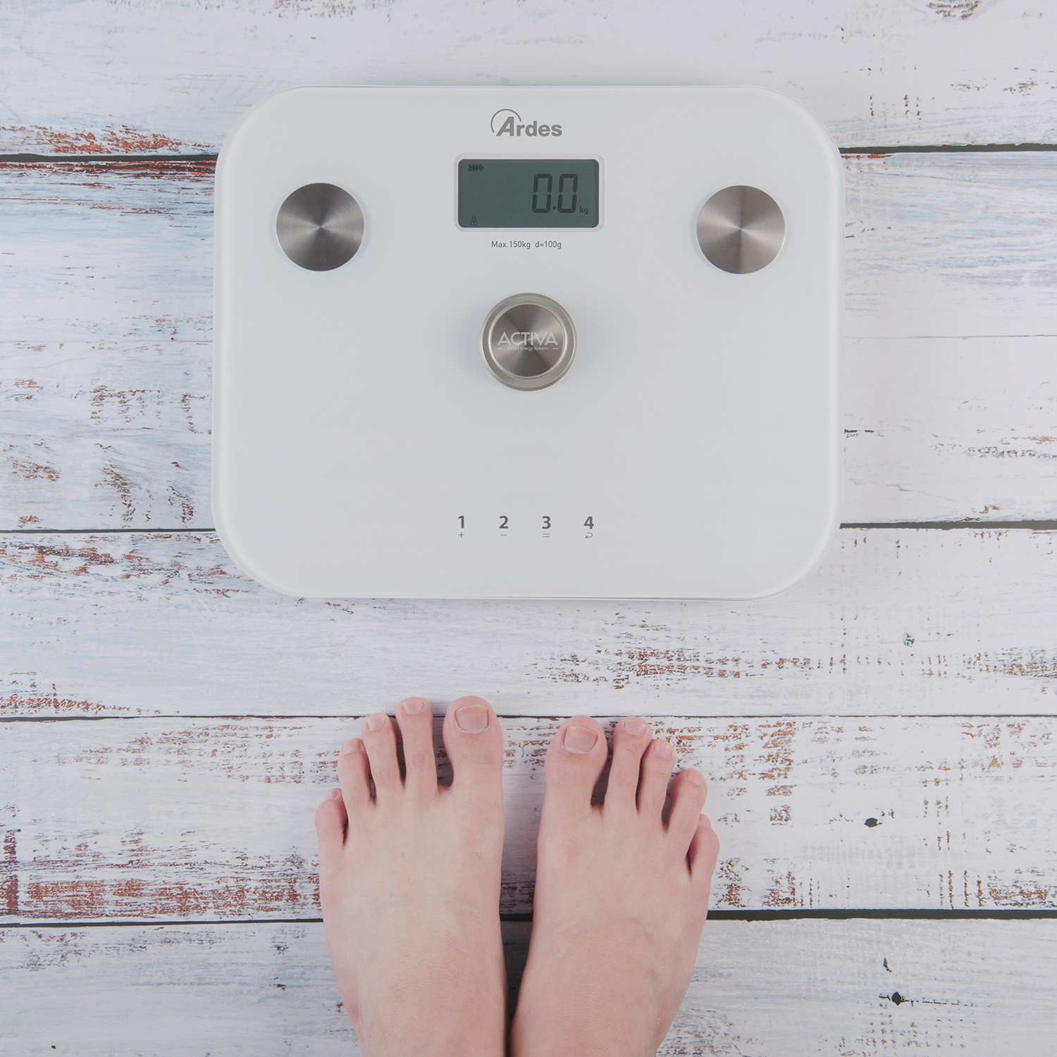 Piedi su una bilancia bianca che mostra 0,0 kg. La bilancia è su assi di legno bianche. La bilancia ha un display digitale e pulsanti.