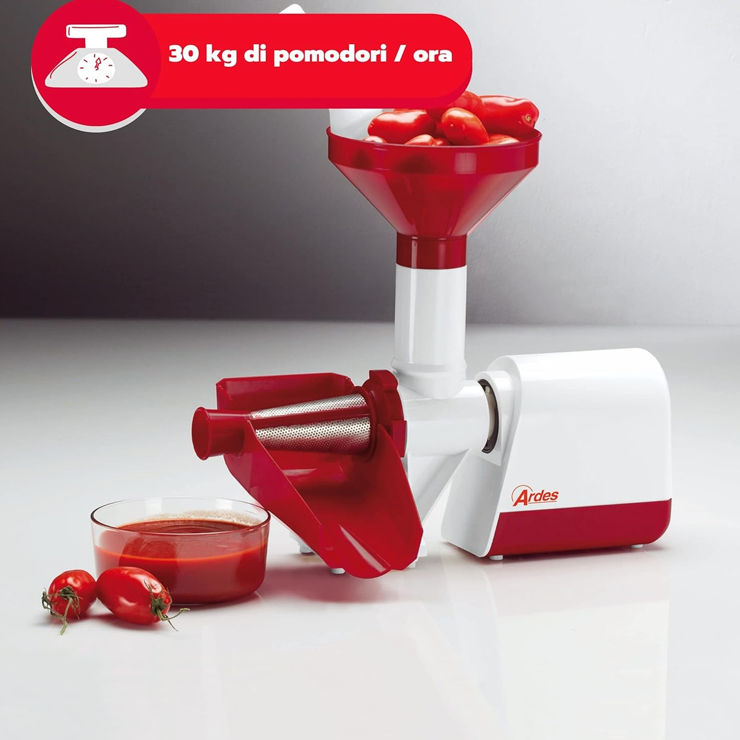 Una macchina per la spremitura dei pomodori bianca e rossa con pomodori nella tramoggia e una ciotola di salsa di pomodoro. La macchina è etichettata Ardes.