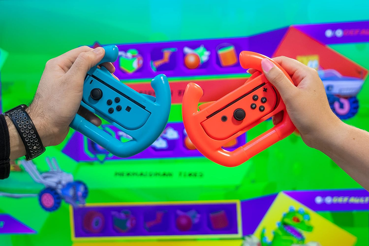 Dos manos sostienen mandos de juego azules y naranjas frente a una pantalla, mostrando iconos de juego. Uno tiene un reloj negro.