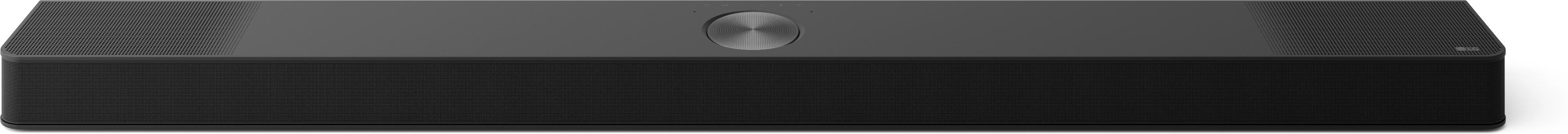 Eine schwarze Soundbar mit einem Mesh-Front und einer perforierten Oberseite. In der Mitte befindet sich ein silberner, kreisförmiger Knopf.