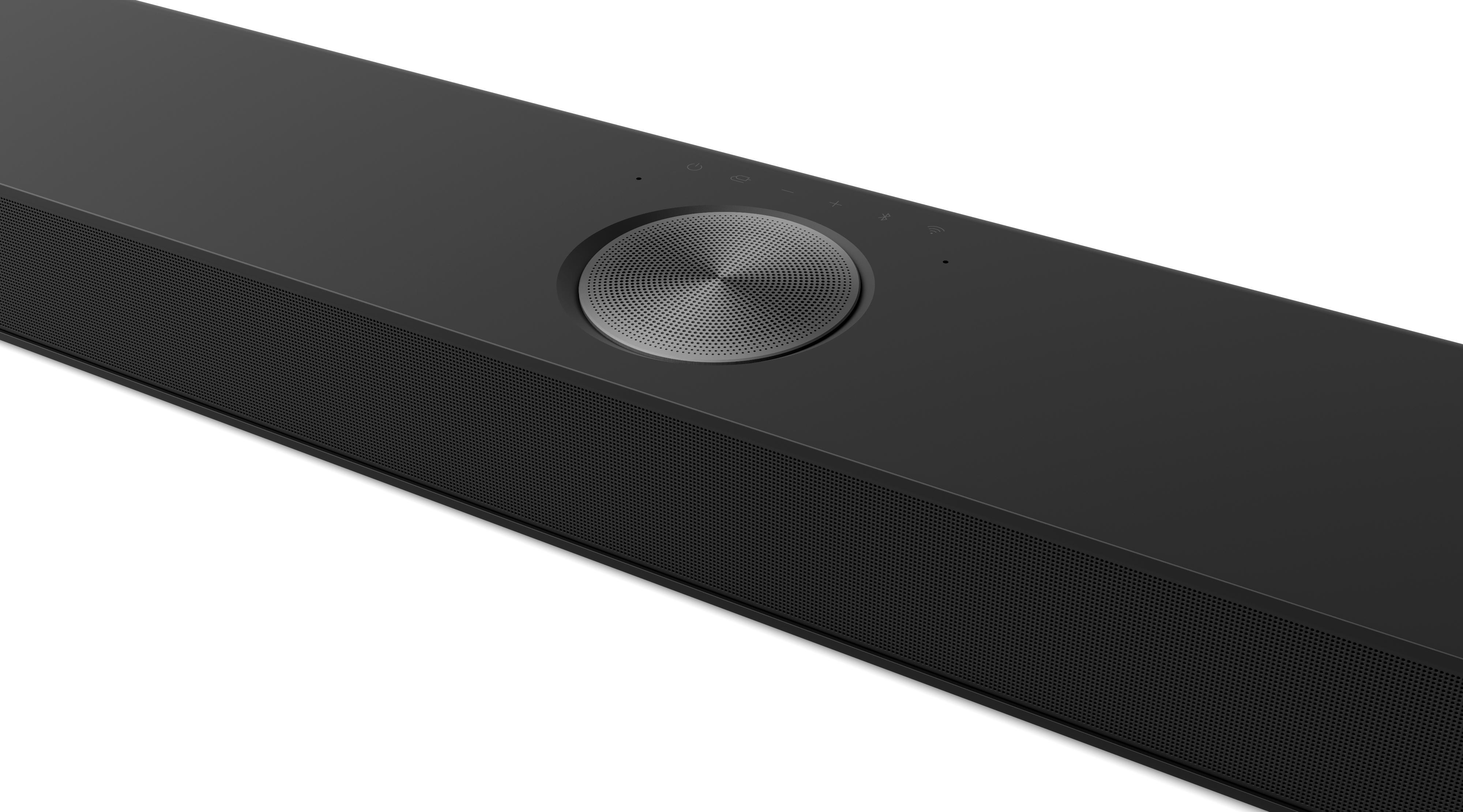 Eine schwarze Soundbar mit einem Mesh-Lautsprechergrill und einem silbernen zentralen Bedienrad. Tasten für Strom, Lautstärke und drahtlose Konnektivität sind sichtbar.