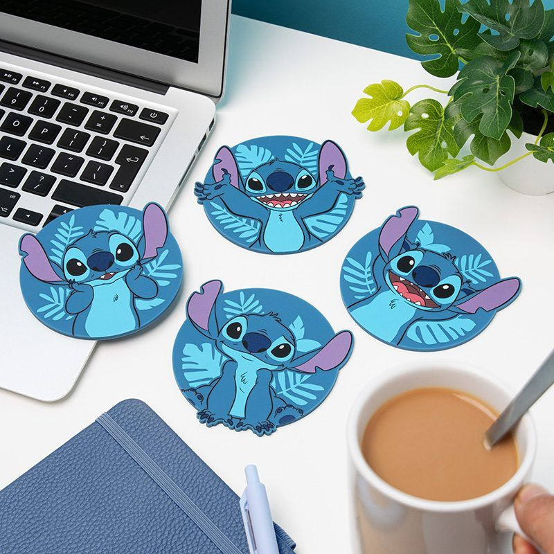Négy Stitch poháralátét, laptop, jegyzetfüzet, toll és kávéscsésze egy fehér asztalon. Növény a háttérben.