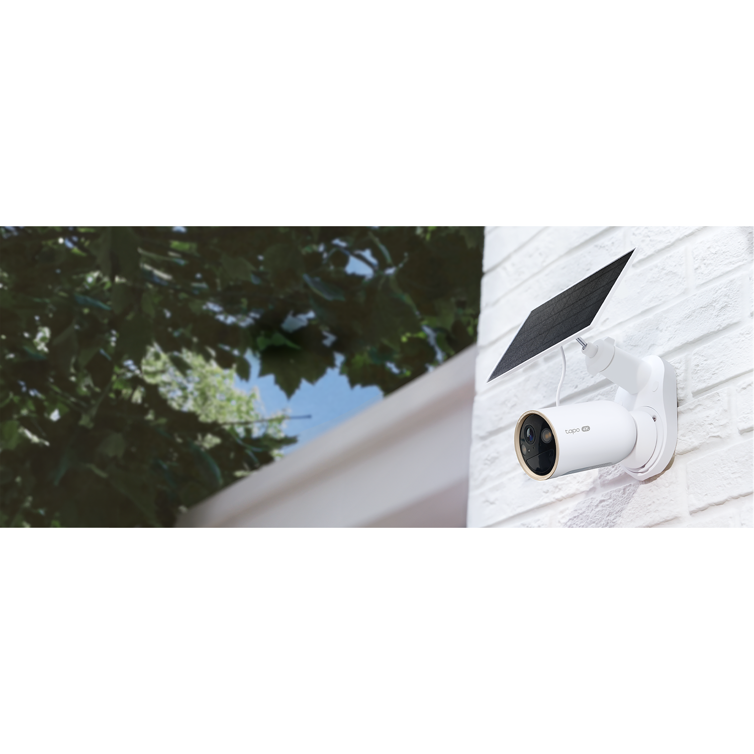 A white security camera with a solar panel, mounted on a white brick wall. Green leaves and blue sky are visible in the background.