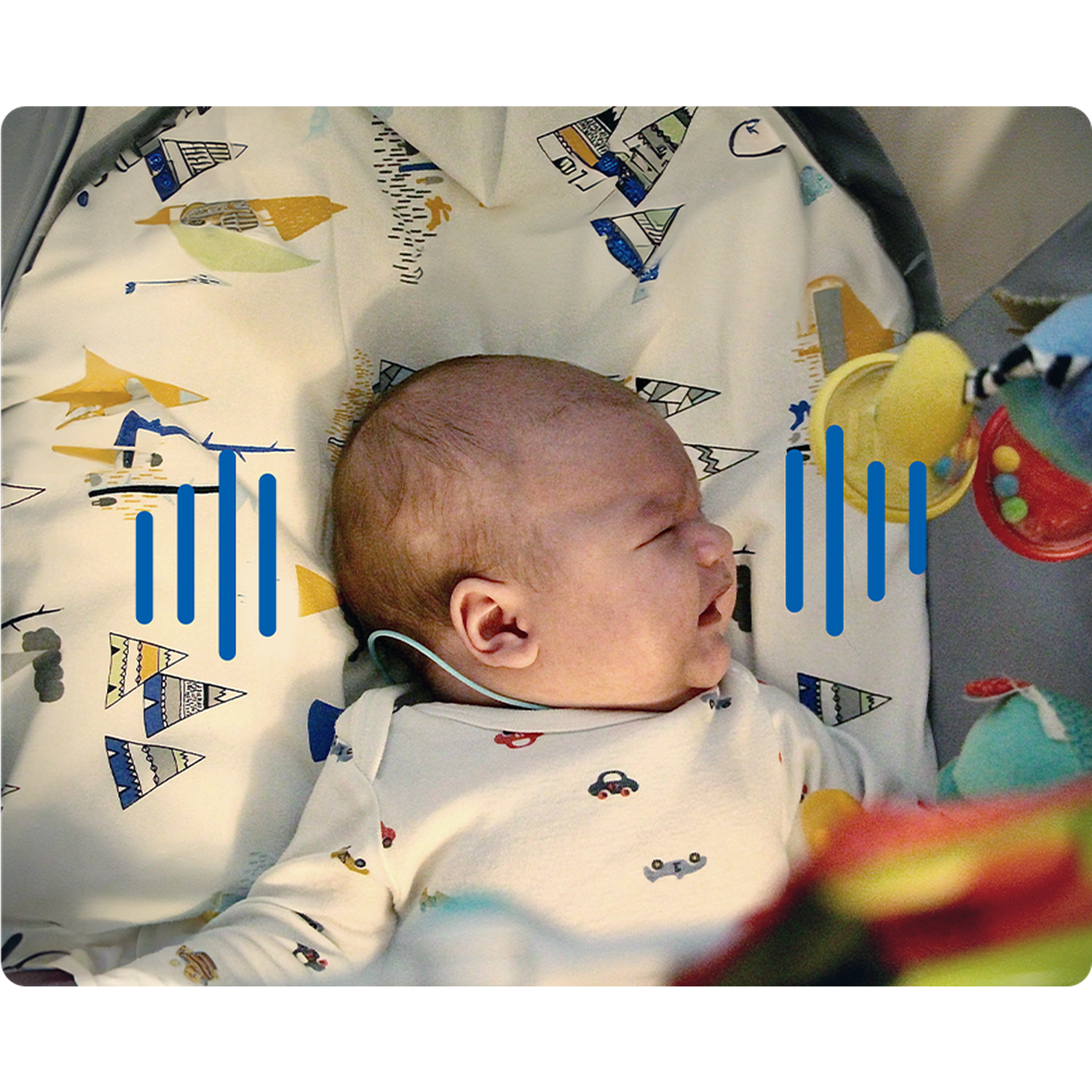 A baby lies on patterned bedding. The baby wears a onesie with car designs. Toys hang above. Blue bars are overlaid.