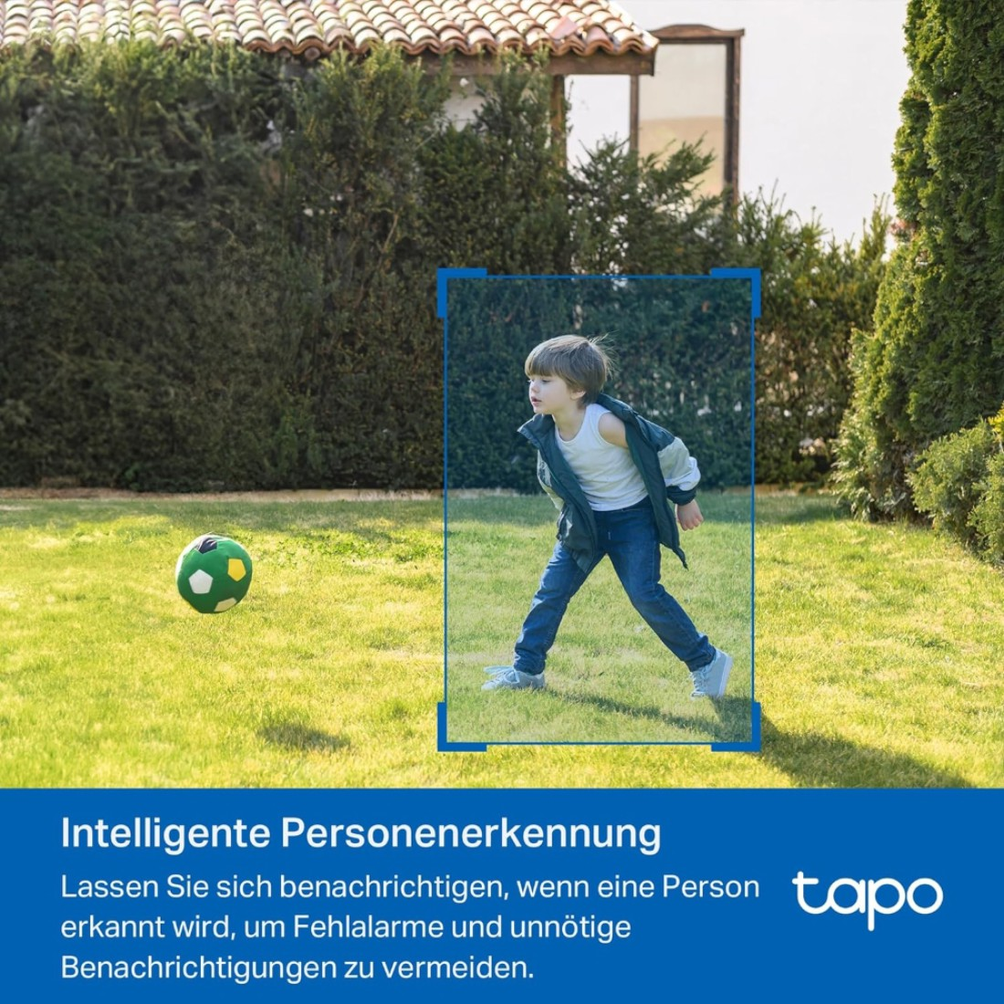 Ein Junge spielt im Garten mit einem Fußball. Er trägt Jeans und eine Jacke. Eine grüne Hecke und ein Haus sind im Hintergrund.