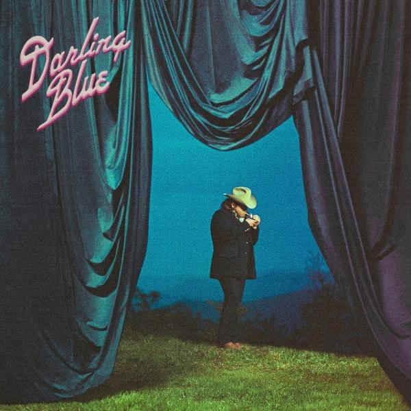 Ein Mann zündet sich eine Zigarette an, trägt einen Hut, vor einem blauen Hintergrund, eingerahmt von dunklen Vorhängen und Gras. Text "Darling Blue".