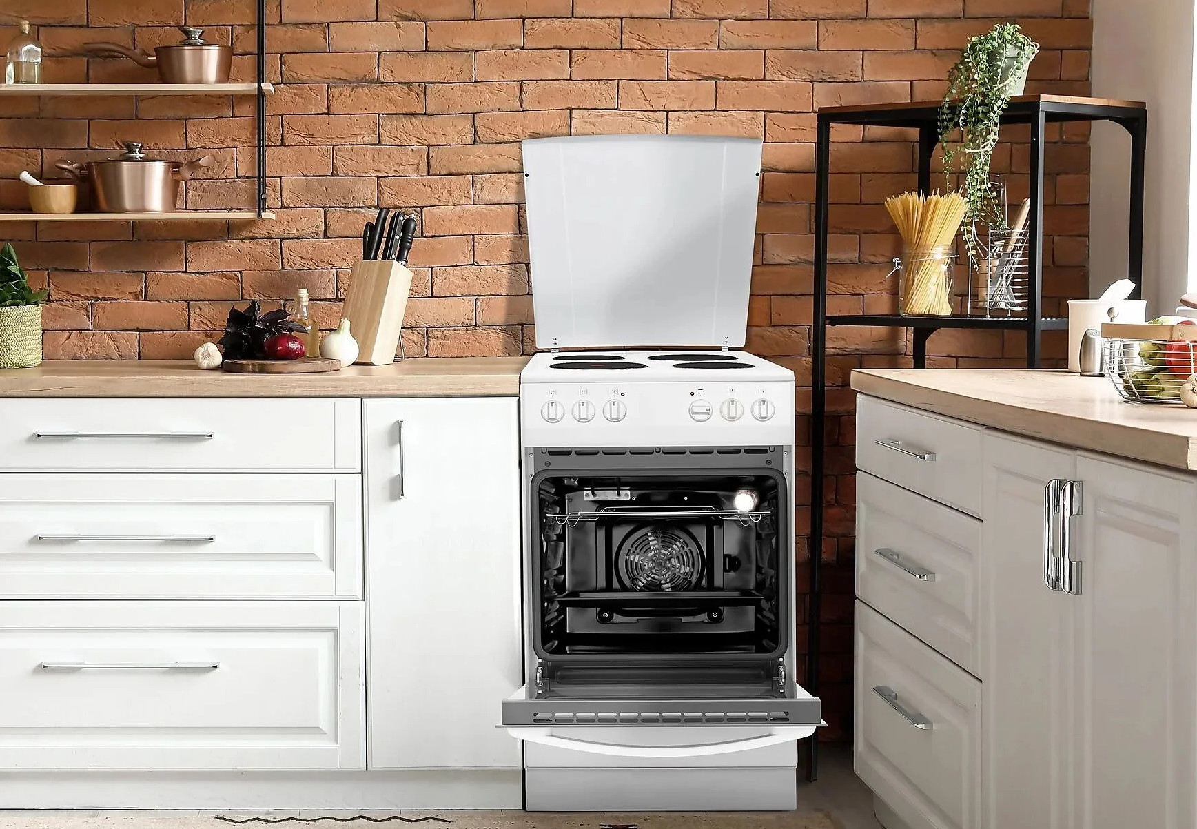 Kuchnia z otwartym białym piekarnikiem. Czerwona ceglana ściana w tle. Białe szafki i drewniany blat.