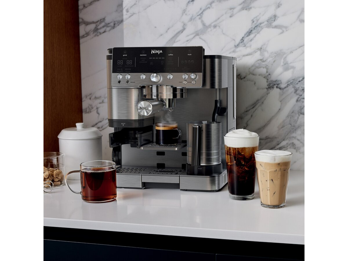 Ekspres do kawy Ninja z napojami kawowymi na białym blacie. Zawiera kawę, filiżankę herbaty i pojemnik na cukier.