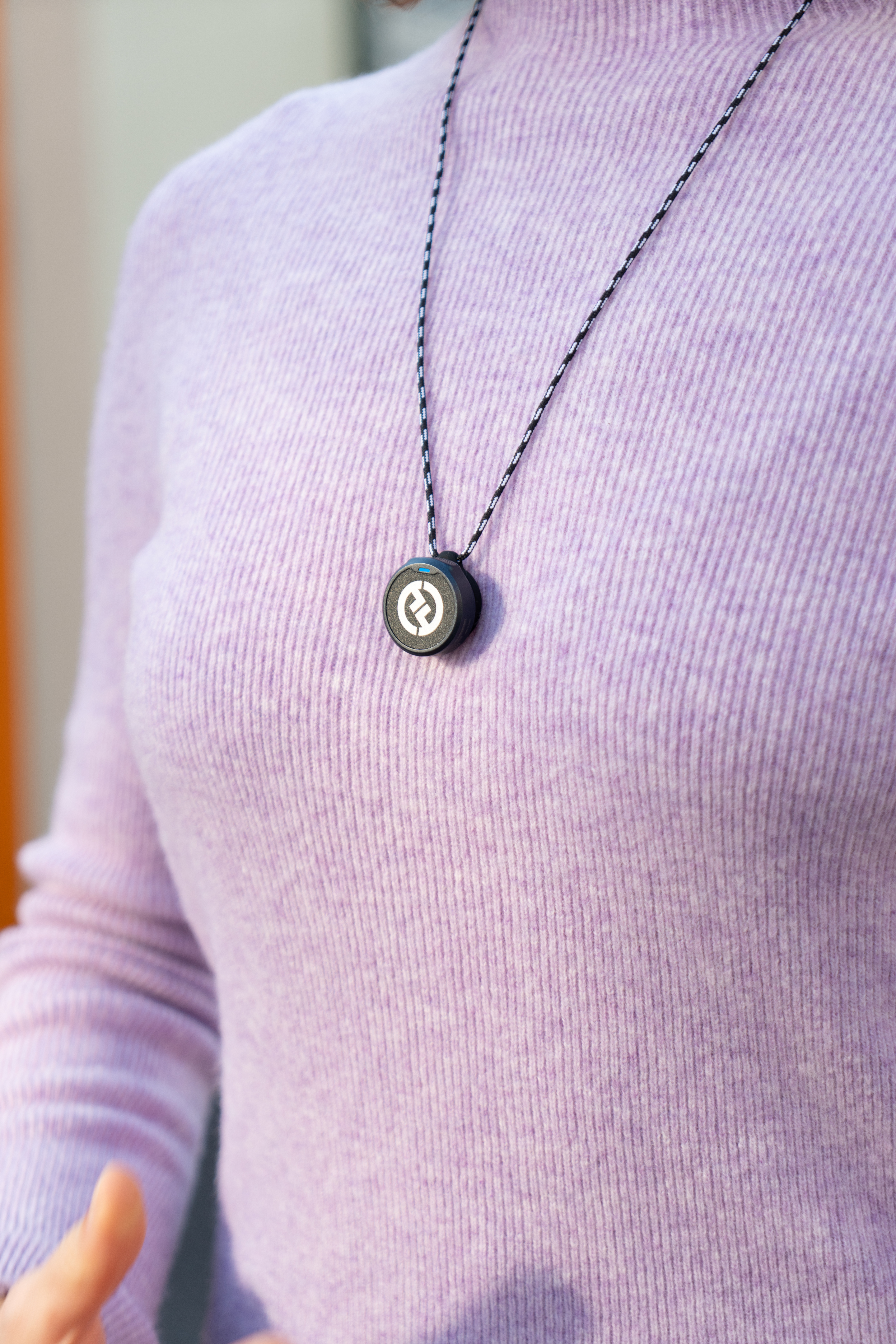 Osoba w liliowym swetrze z naszyjnikiem ze sznurkiem czarno-białym i okrągłą czarną zawieszką.