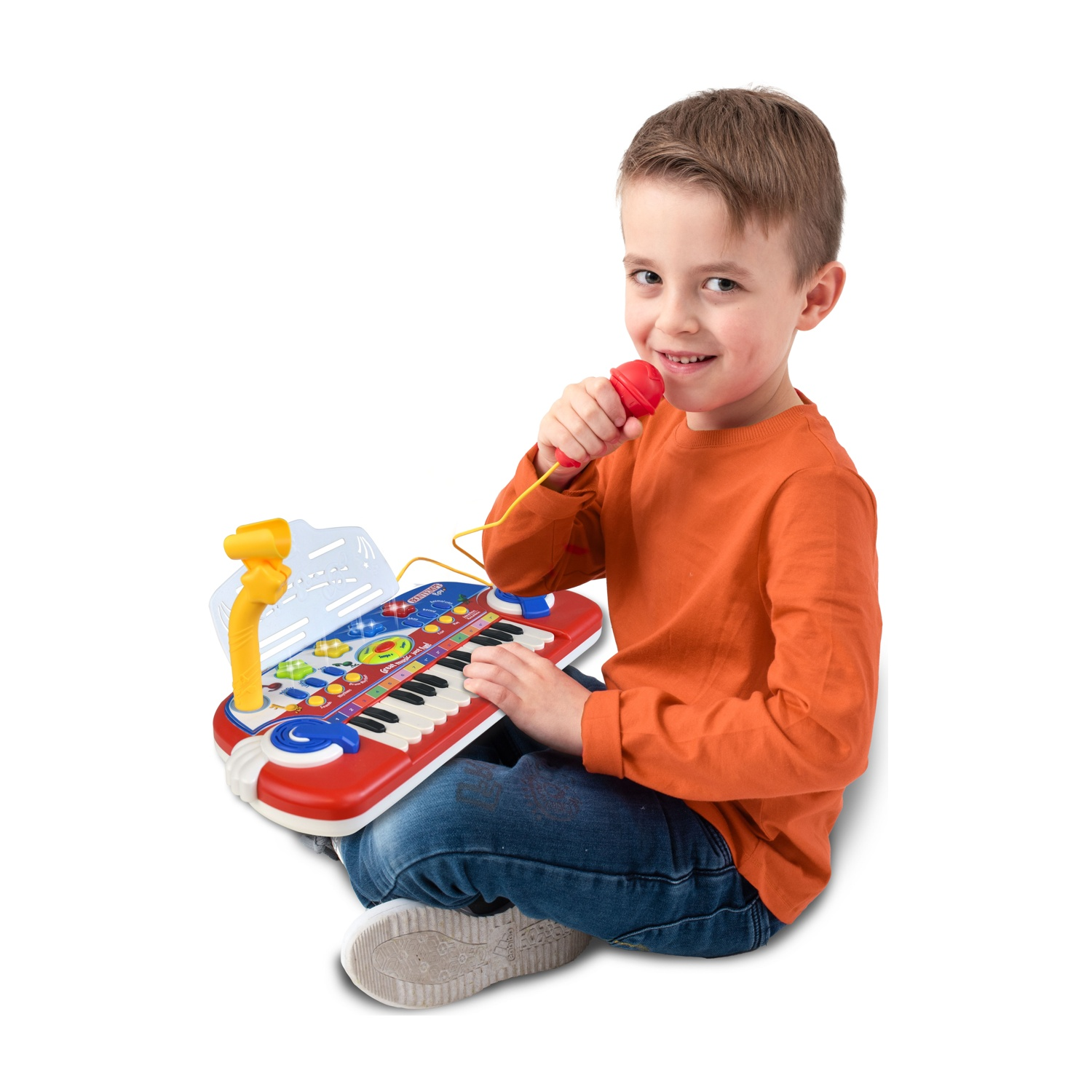 Un bambino seduto tiene un microfono rosso e un pianoforte giocattolo. Sorride, indossa una maglietta arancione e jeans.
