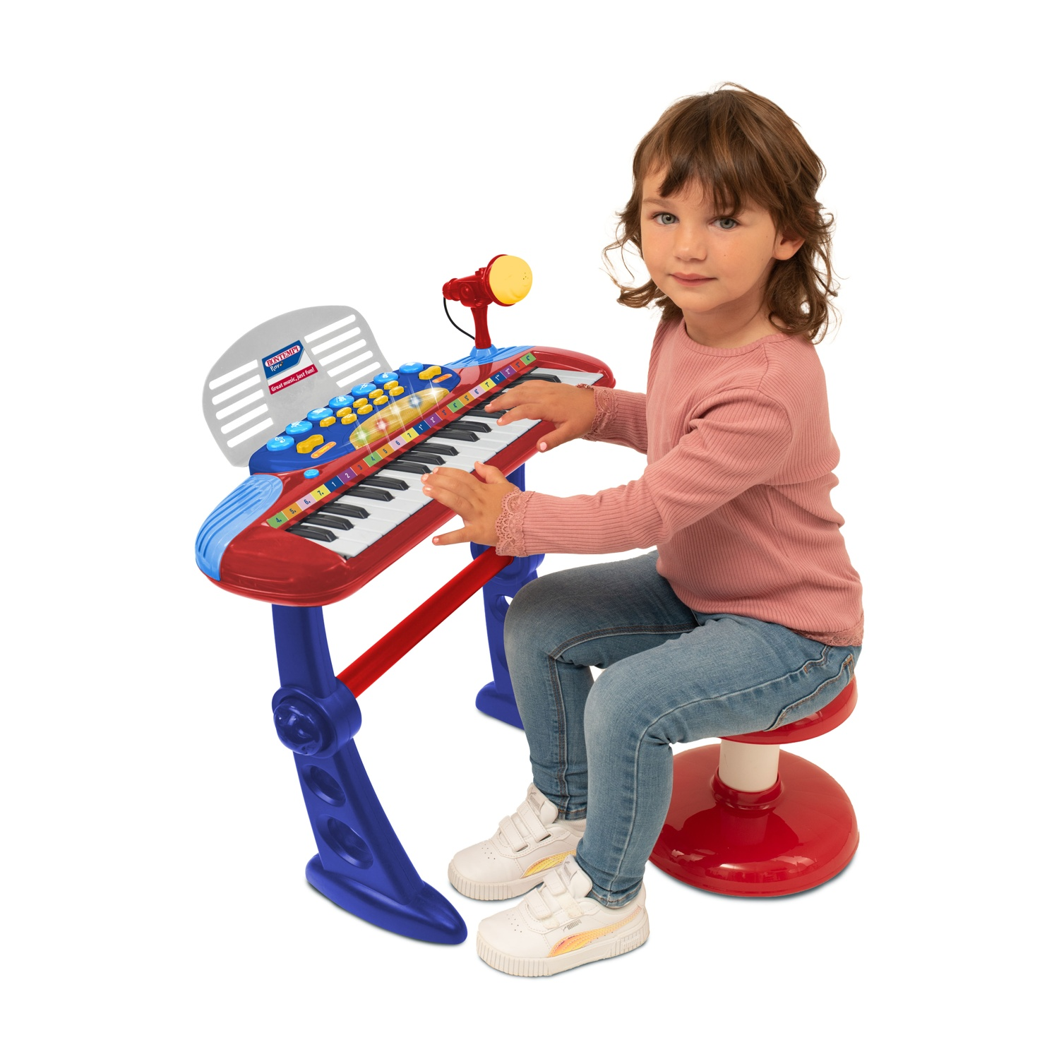 Una bambina è seduta a un pianoforte giocattolo, che suona. Indossa una camicia rosa e jeans ed è su uno sgabello rosso. Il pianoforte è rosso e blu.