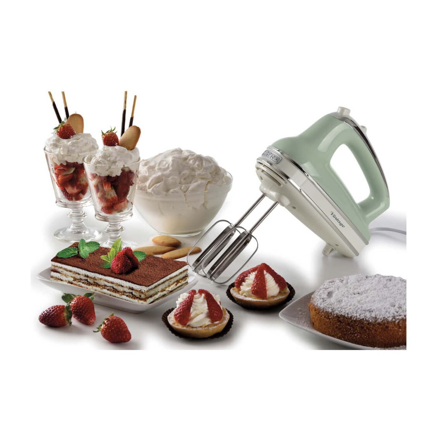 Un mixer e dessert su una superficie bianca. Ci sono parfait, una torta e pasticcini con fragole. È presente anche panna montata.