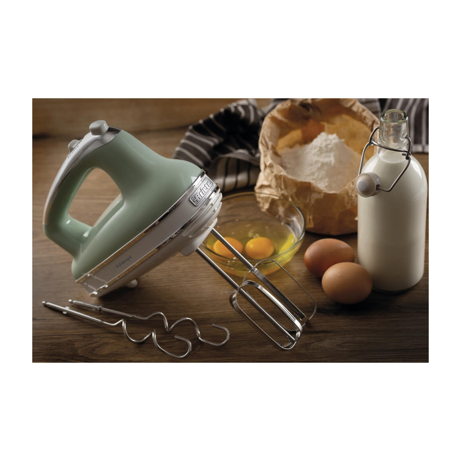 Un mixer vintage verde su una superficie di legno. Uova, farina e latte nelle vicinanze, suggeriscono la cottura.