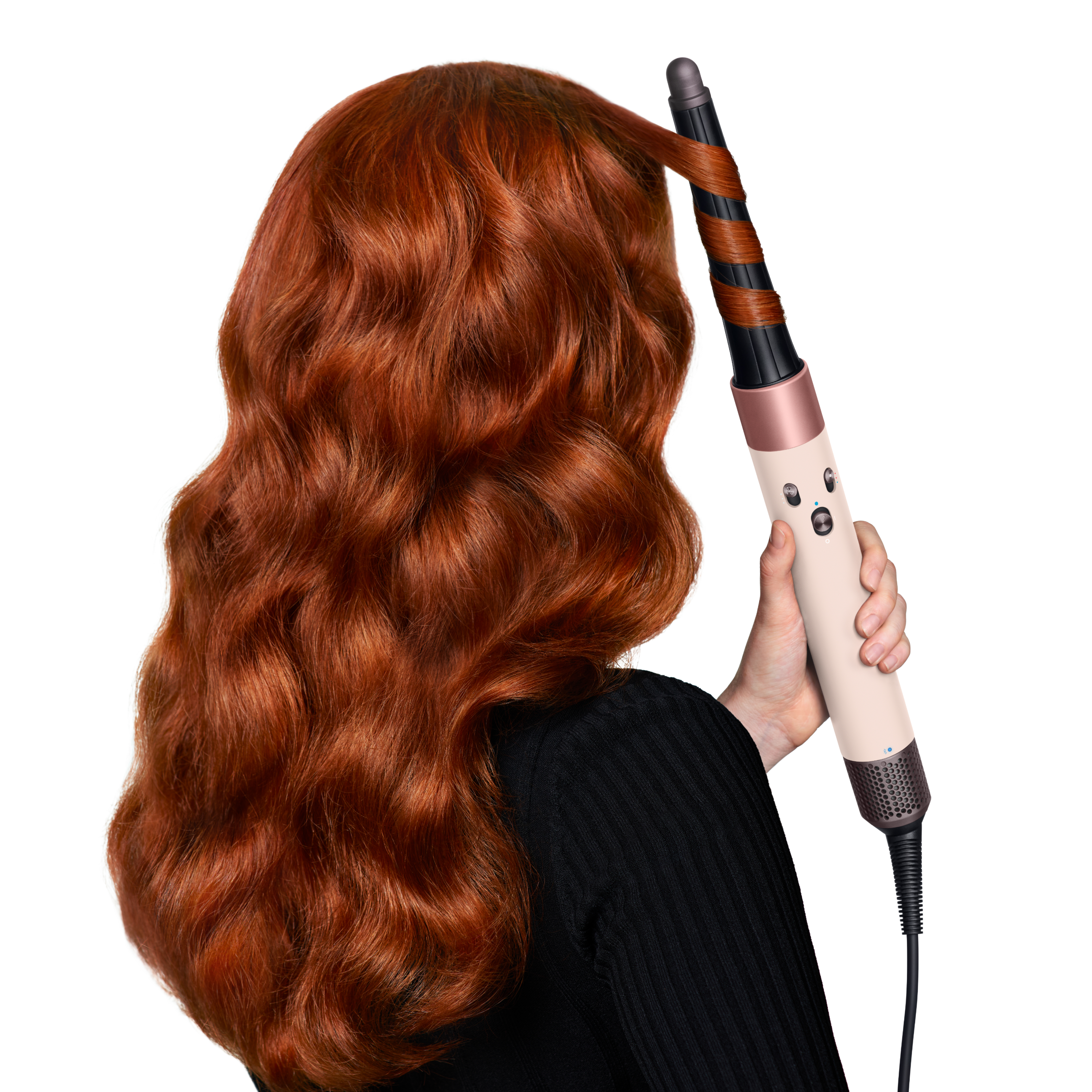 Mujer con pelo rojo usando un rizador. El pelo se está peinando. Lleva una blusa negra. Fondo blanco.