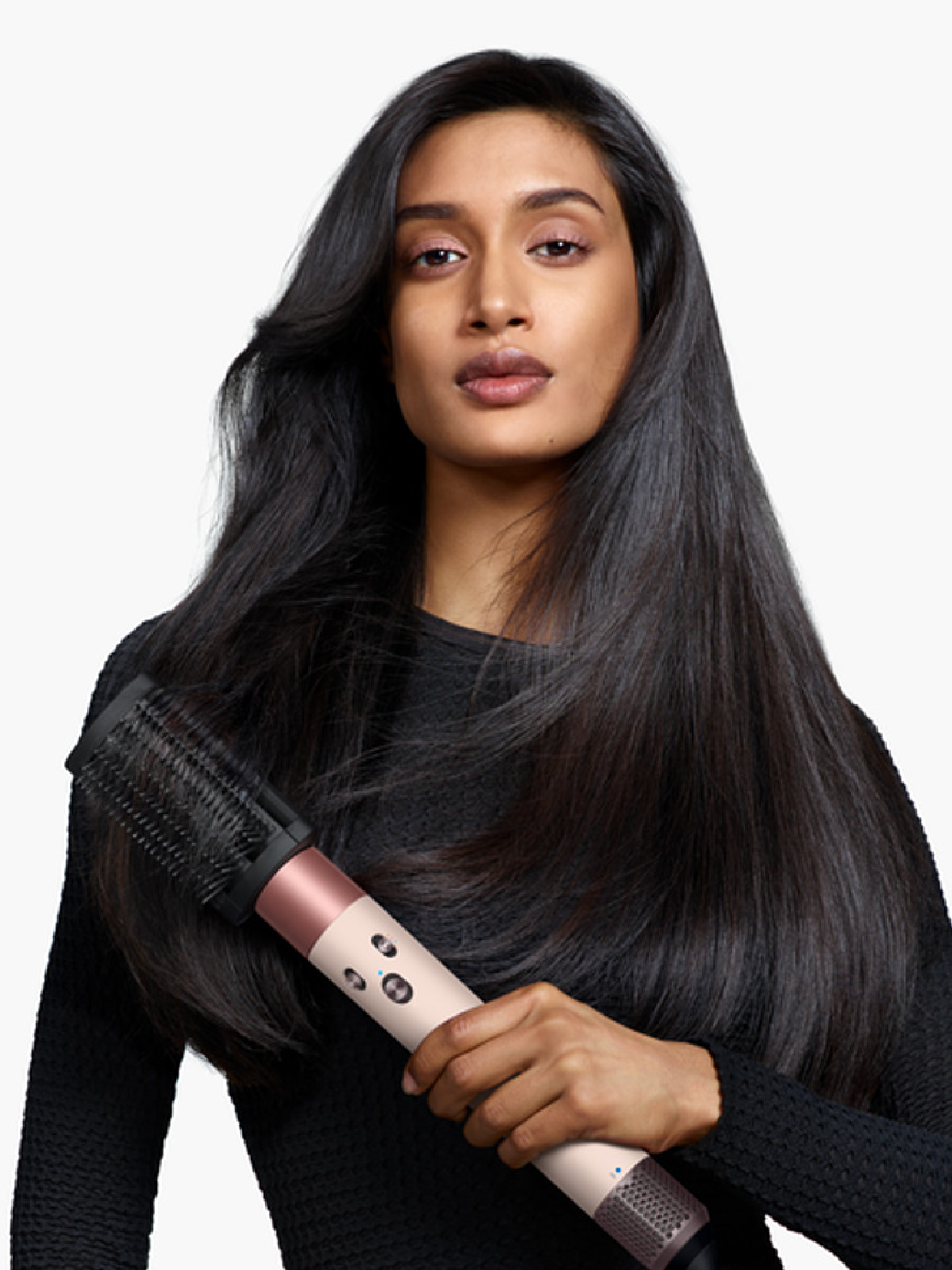 Una mujer con largo cabello negro sostiene una herramienta rosa y negra para peinar. Lleva una blusa negra, y el fondo es blanco.