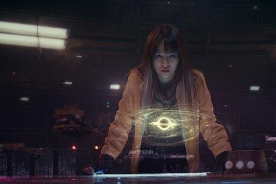 Frau mit orangefarbener Jacke betrachtet ein holografisches schwarzes Loch.