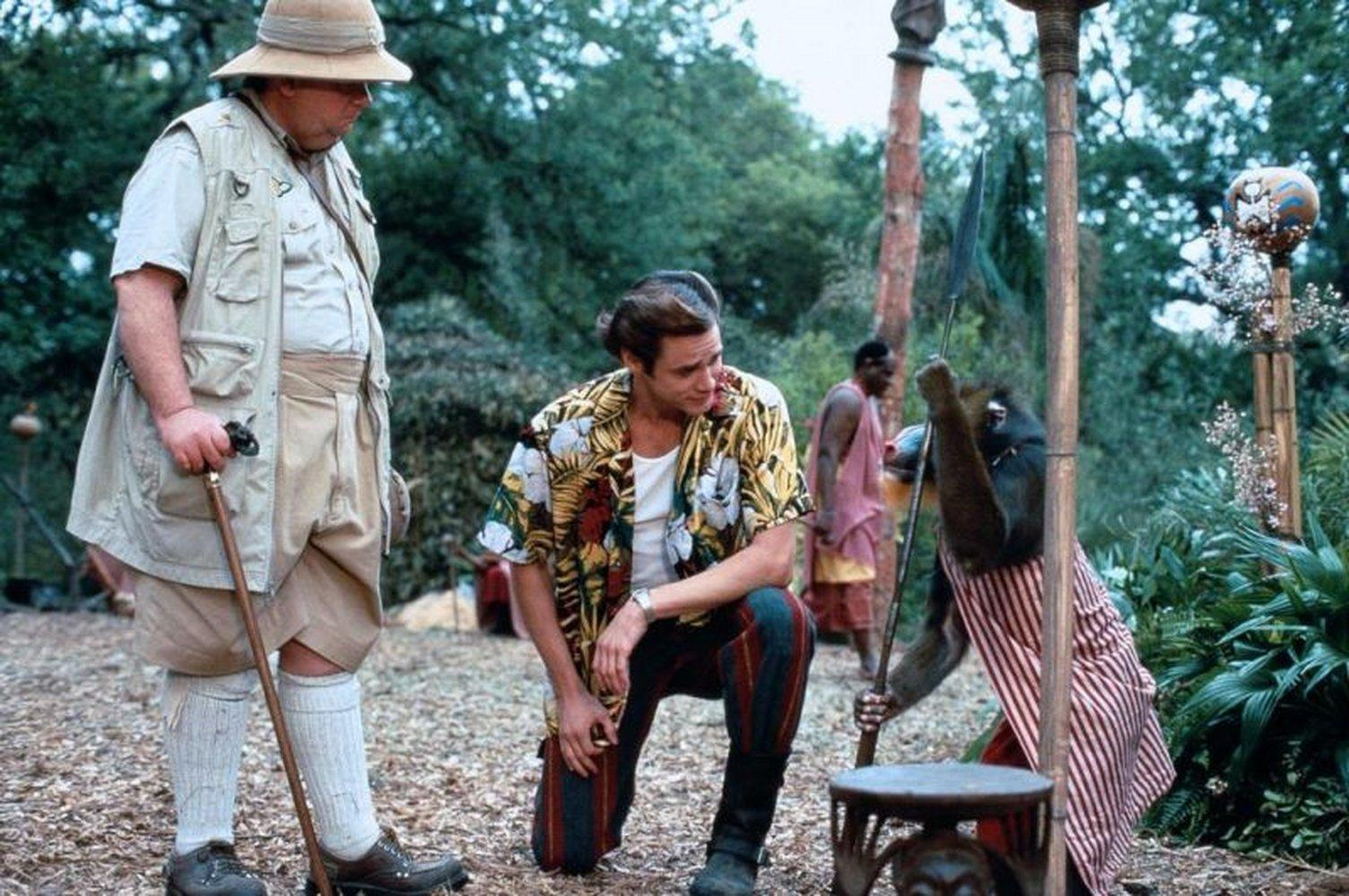 Männer in Safari-Kleidung und Hemd mit Blumenmuster mit einem Affen in einer gestreiften Schürze, der einen Speer hält. Dschungel-Kulisse.