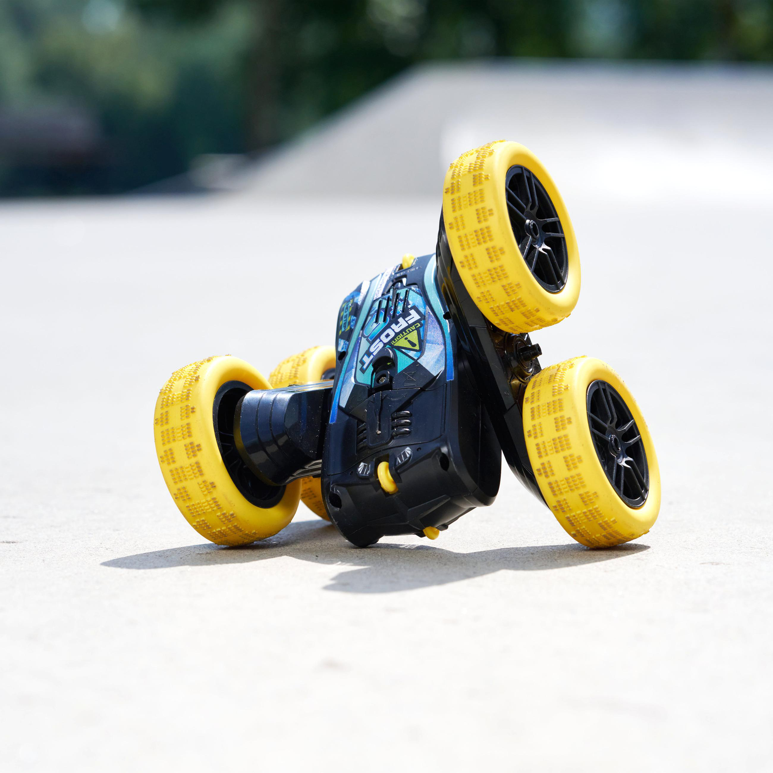 Ein schwarz-blaues Spielzeugauto mit gelben Rädern steht auf einer Betonoberfläche, im verschwommenen Hintergrund Bäume.