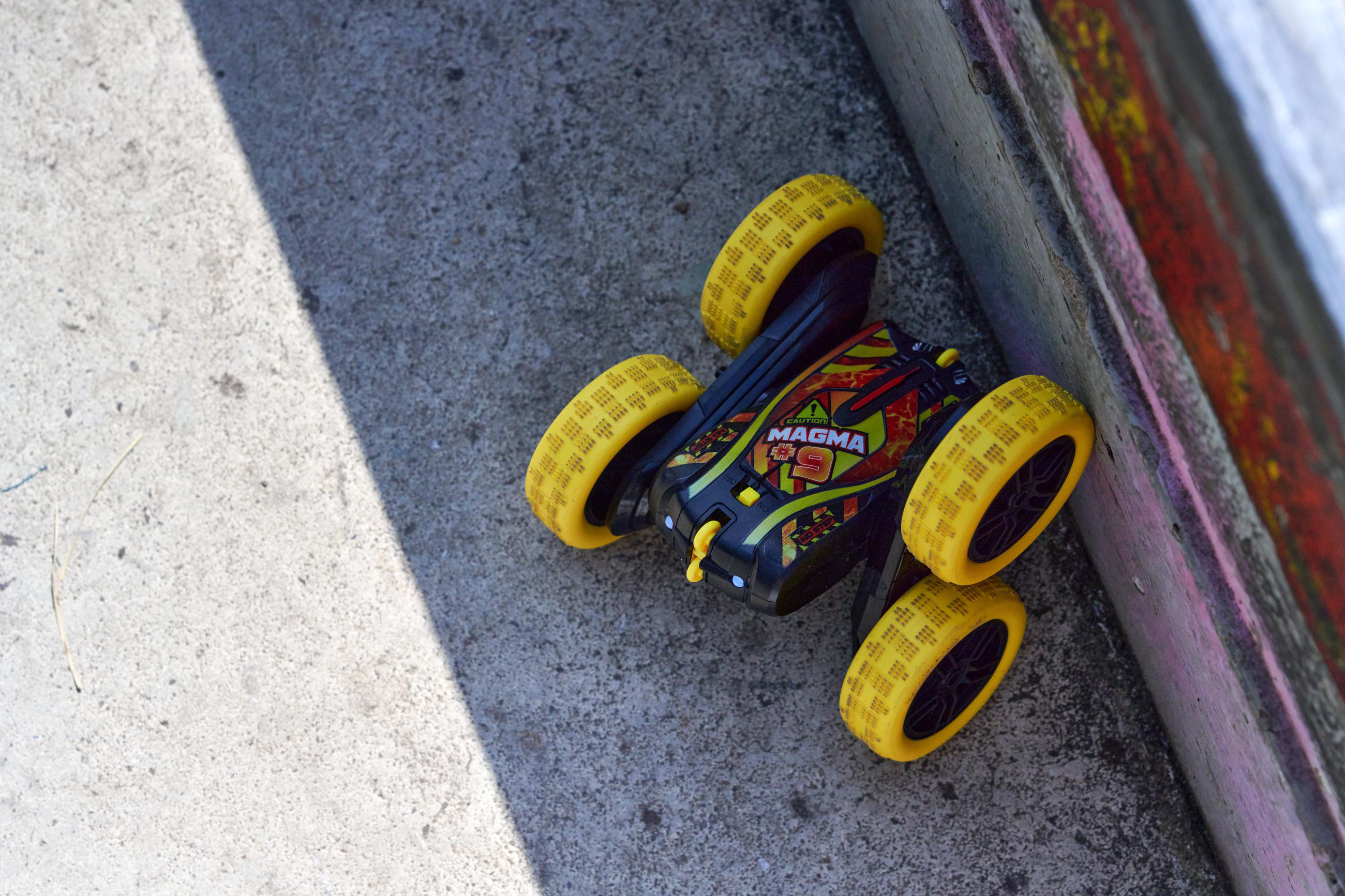 Ein schwarz-gelbes Spielzeugauto auf einer Betonoberfläche. Es hat gelbe Räder und steht neben einer bemalten Wand.