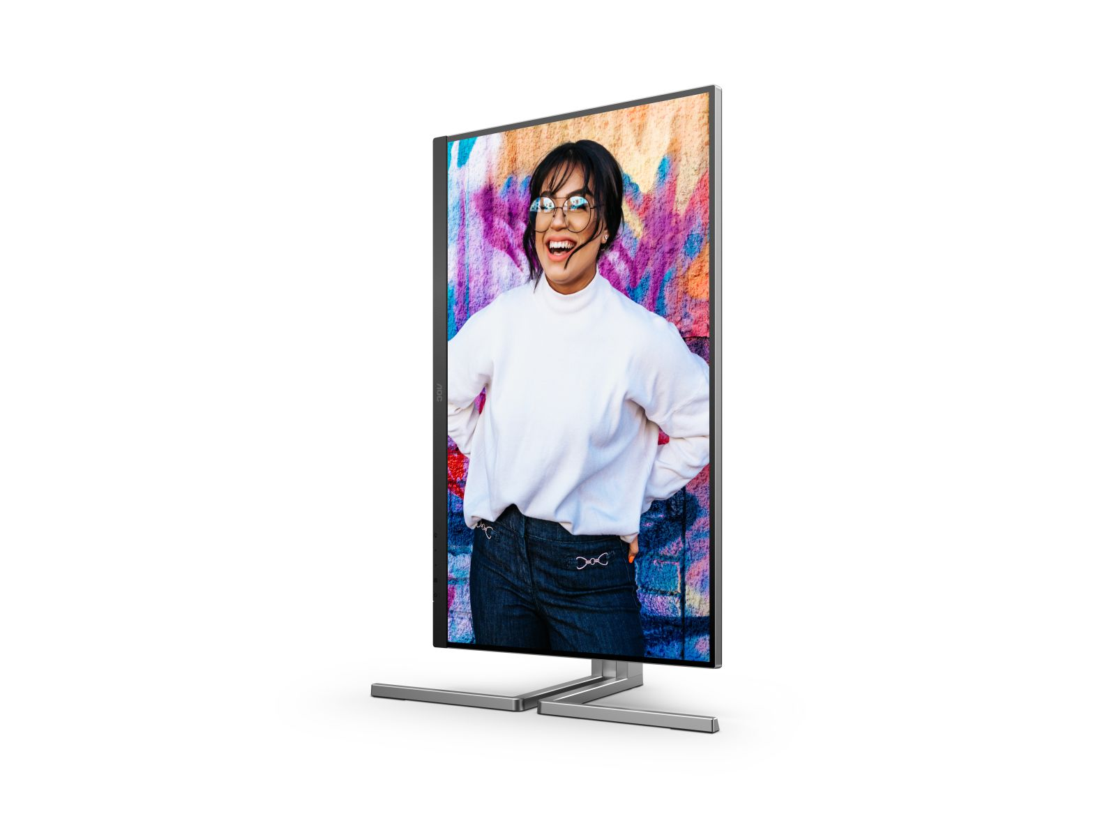 Un monitor muestra a una mujer sonriente con gafas. Lleva un suéter blanco y jeans. El fondo es un graffiti colorido.