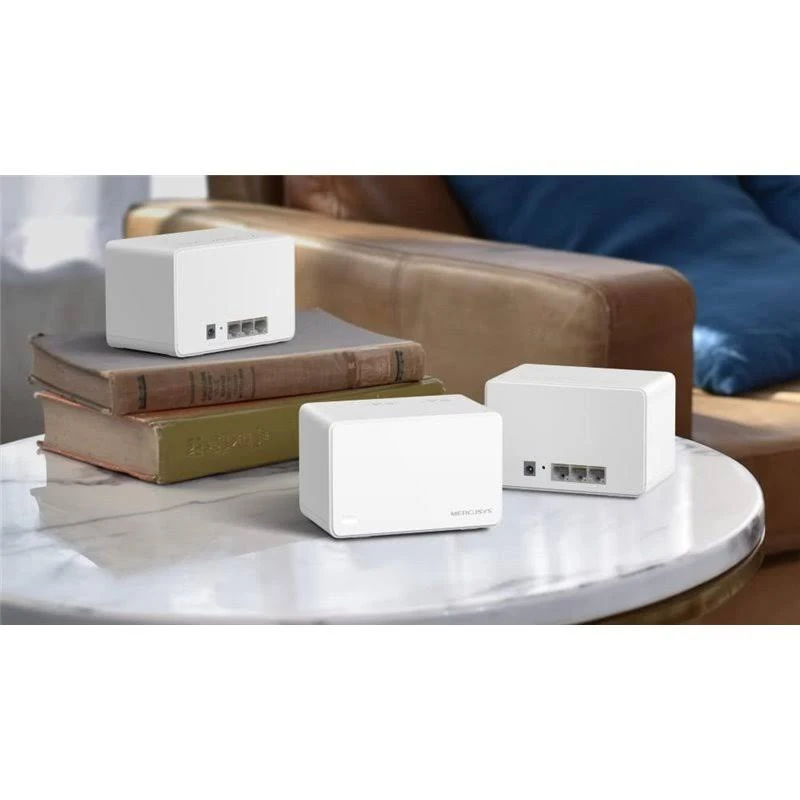 Tres routers blancos sobre una mesa de mármol, uno sobre libros, cerca de un sofá de cuero. Los routers tienen puertos visibles. Fondo desenfocado.