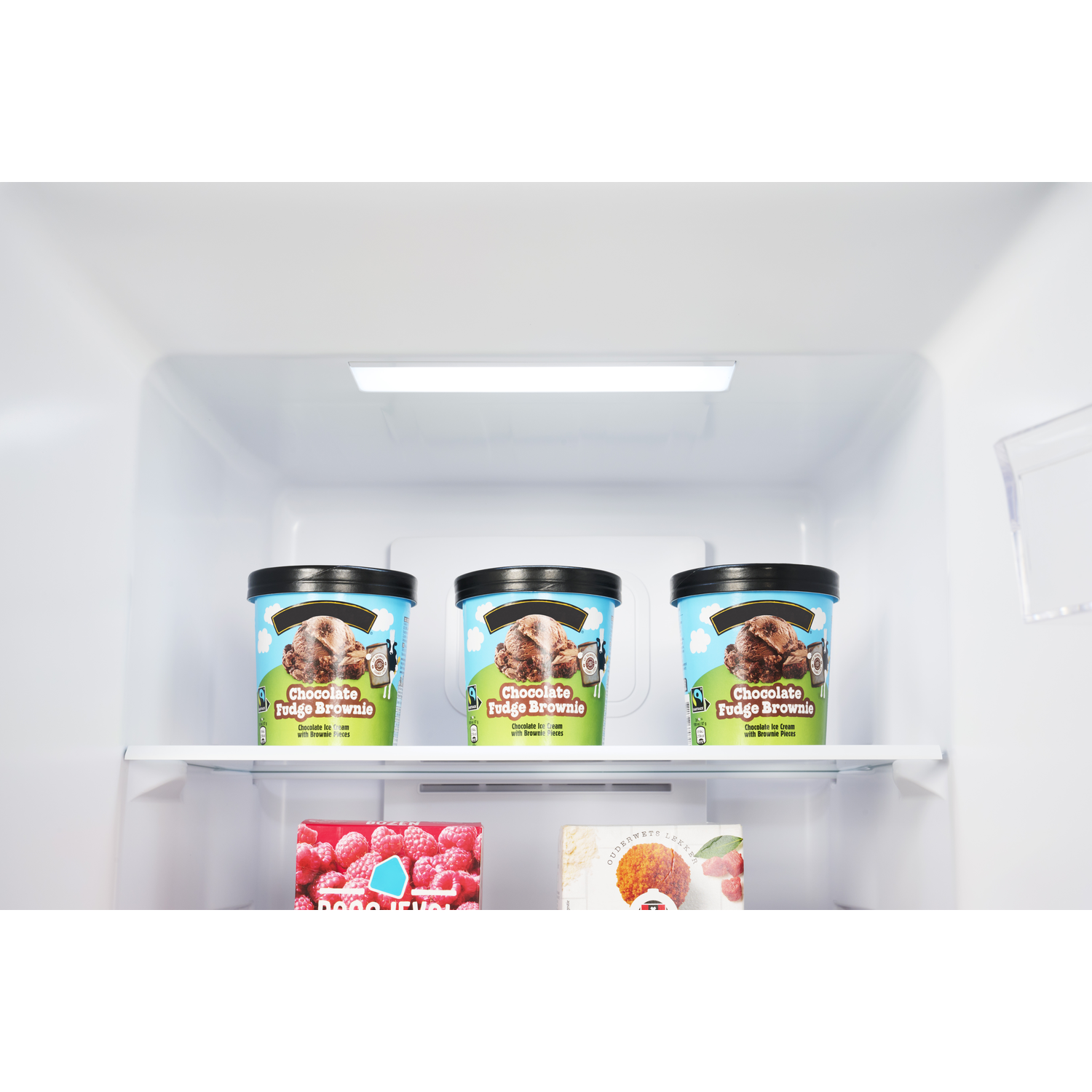 In een koelkast staan ​​drie ijsbakjes met het label "Chocolate Fudge Brownie" op een plank. Daaronder bevinden zich dozen met diepvriesproducten.