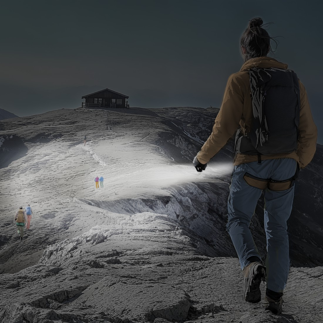 Eine Person wandert auf einem schneebedeckten Berg und leuchtet mit einer Taschenlampe. Andere Wanderer gehen auf eine Hütte zu. Dunkler Himmel.
