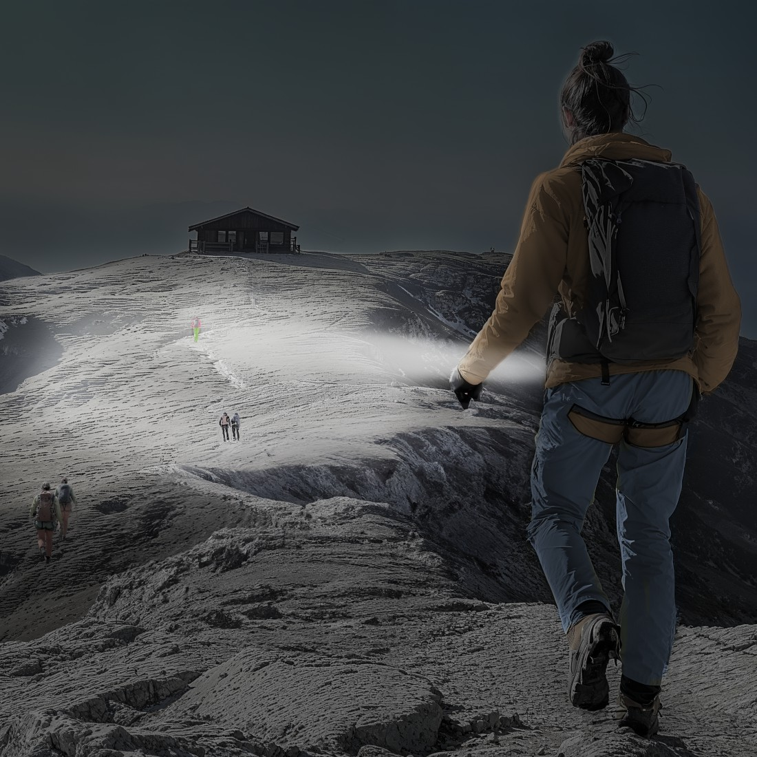 Ein Wanderer mit Rucksack und Stirnlampe führt den Weg auf einem verschneiten Bergpfad zu einer Hütte. Andere Wanderer folgen.