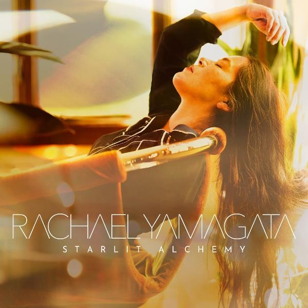 Eine Frau lehnt sich in einem Stuhl zurück, der Kopf ist nach hinten geneigt. Lange Haare, schwarzes Oberteil. Der Text lautet Rachael Yamagata, Starlit Alchemy.