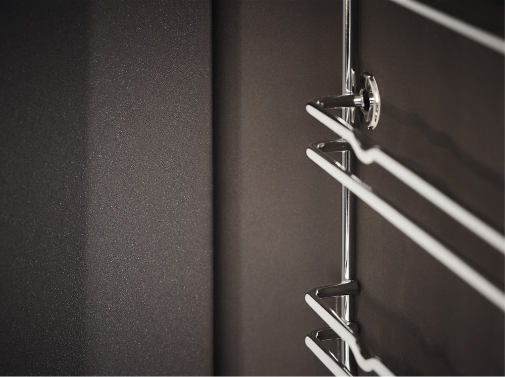 Zbliżenie pokazuje chromowany wieszak na ręczniki na ciemnobrązowej ścianie. Lewa strona ma teksturowaną, ciemną powierzchnię.